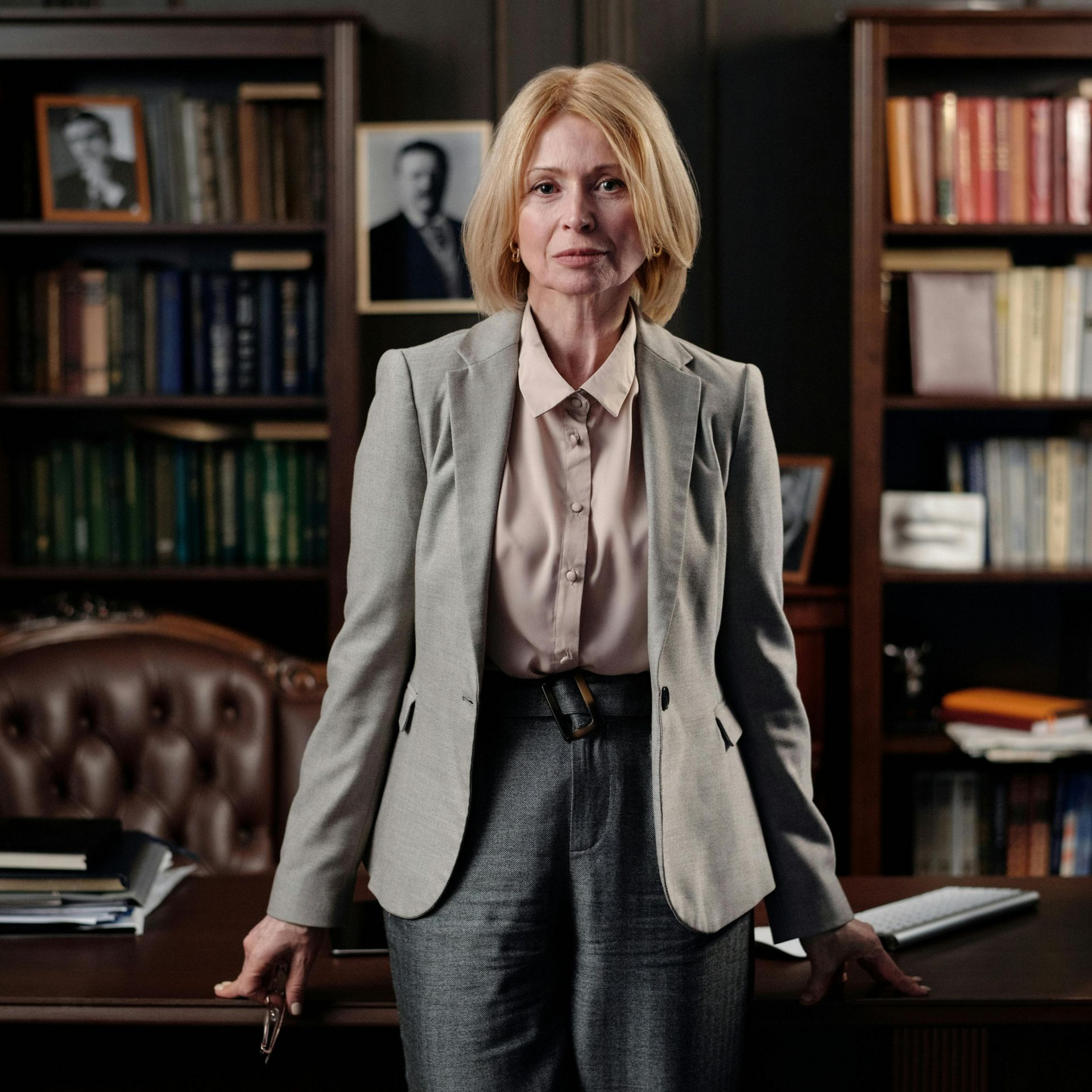 Woman in gray suit, standing behind a desk in a library, looking directly at the camera.