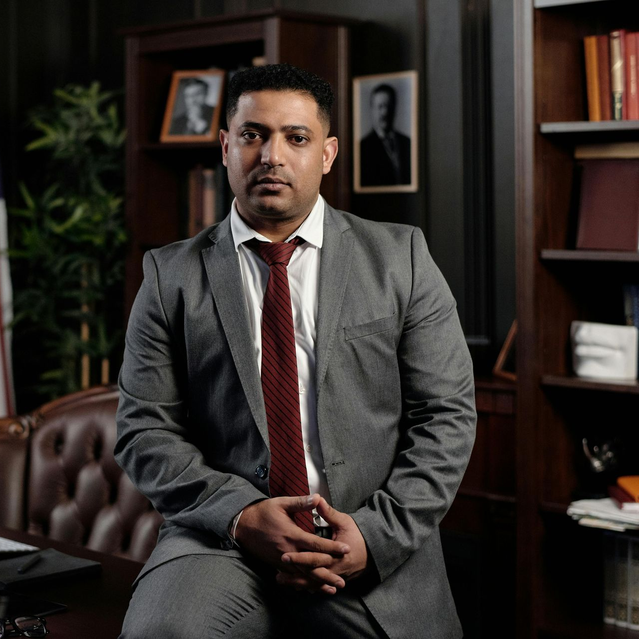 Man in suit and tie seated in office, arms crossed.