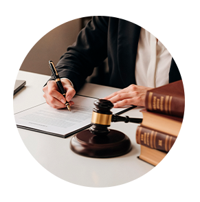 A person in a blazer signing a document at a desk with a gavel and law books.