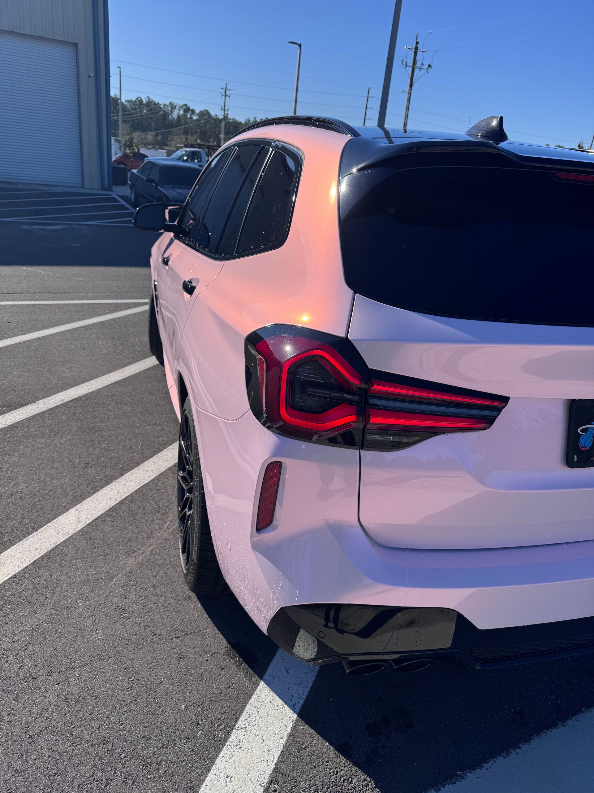 Pink iridescent SUV parked outdoors. Black tinted windows, black rims, and a sunny day.