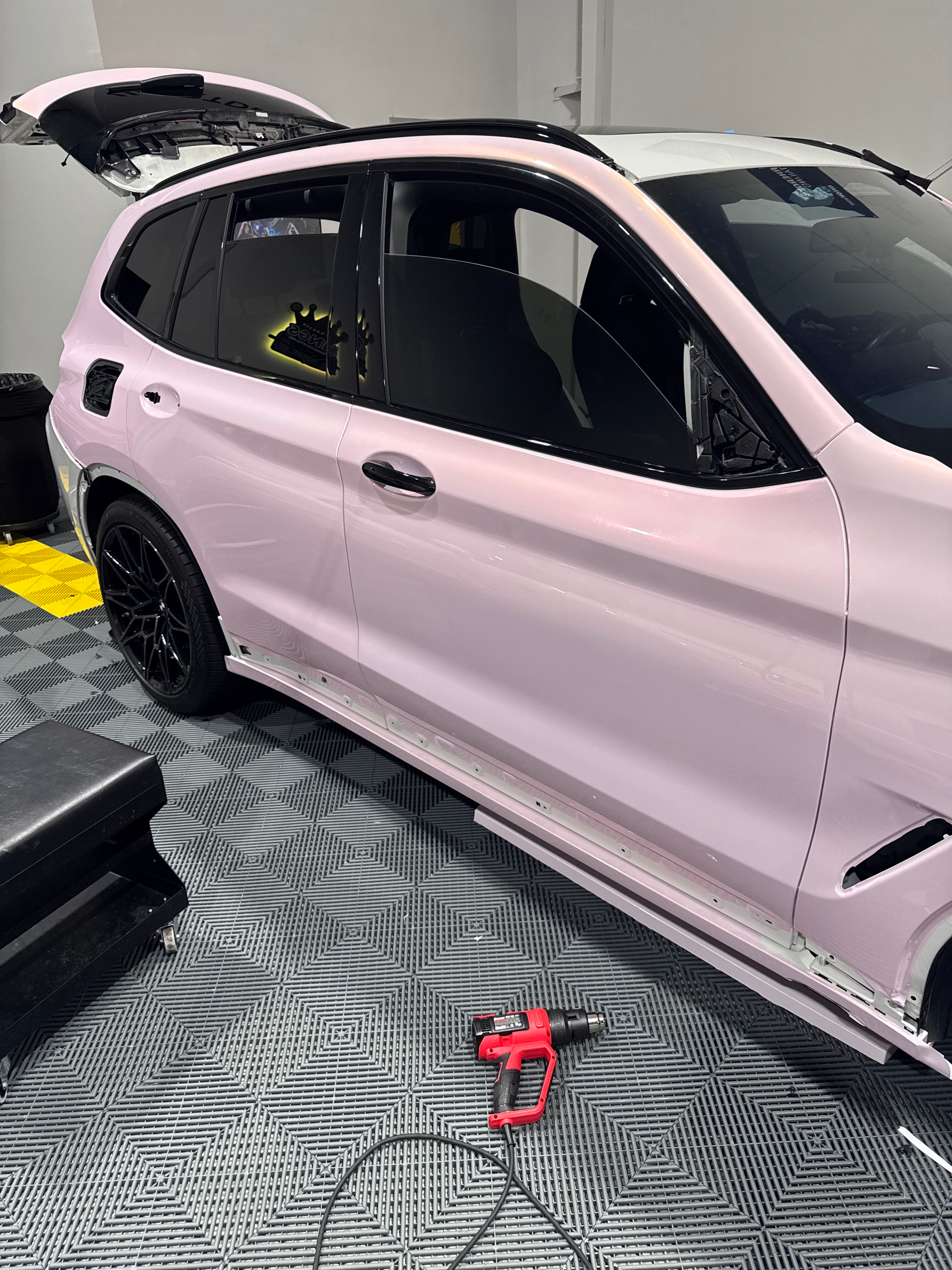 Pink SUV parked in a shop, with a heat gun on the ground.