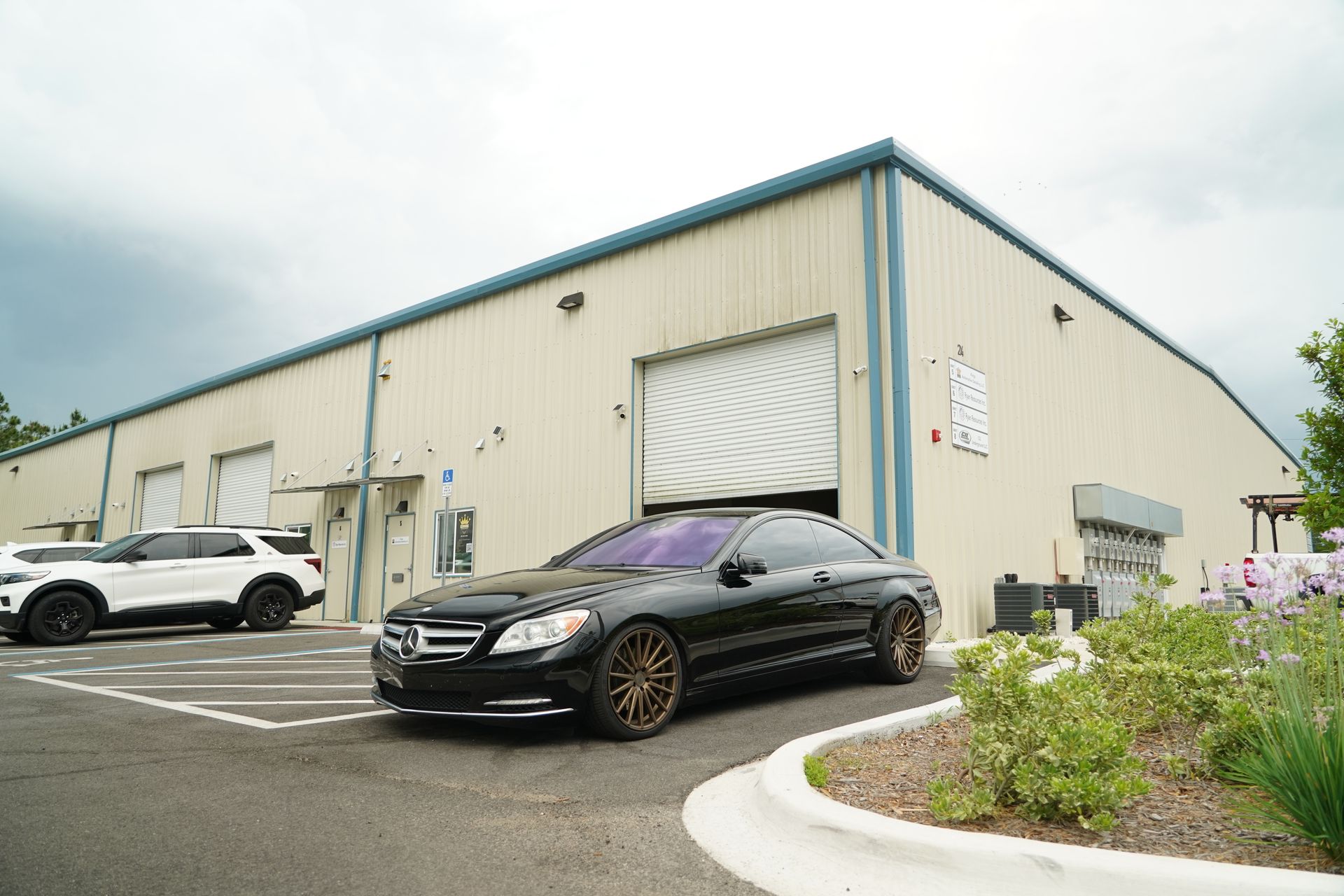 Black car parked in front of a tan industrial building with open garage door.