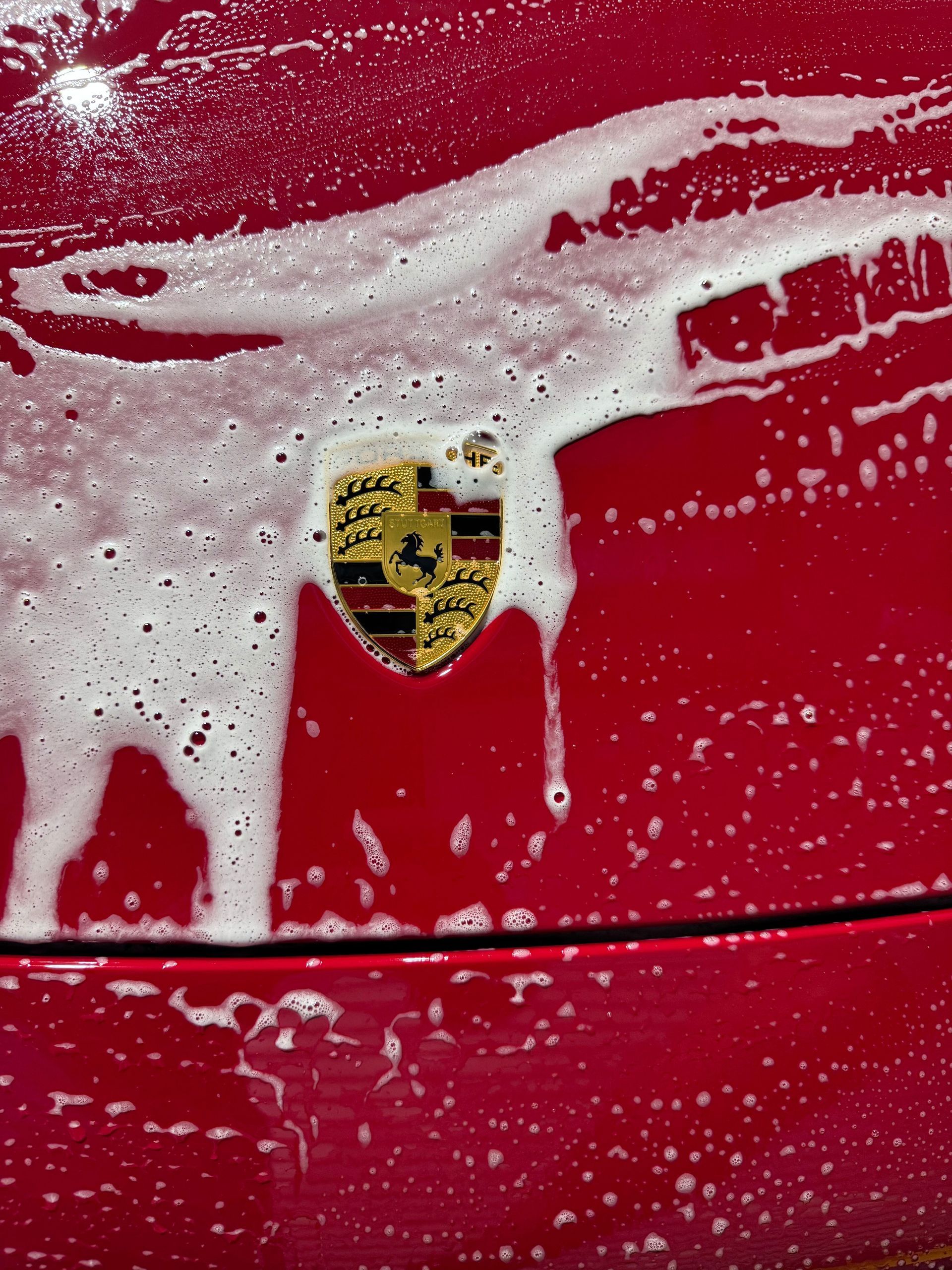 Red Porsche car with soapy foam over the hood, centered on the car's logo.