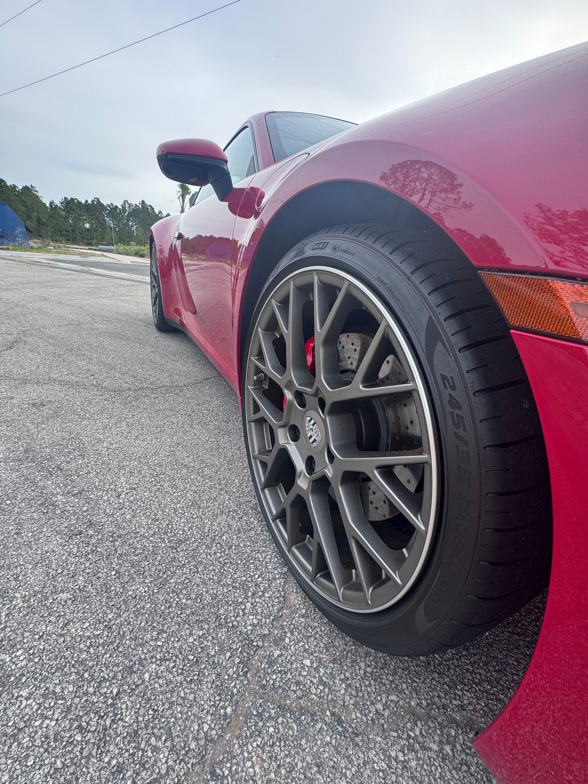 Red sports car, close-up of the front wheel and body, on a gray asphalt surface, cloudy sky.