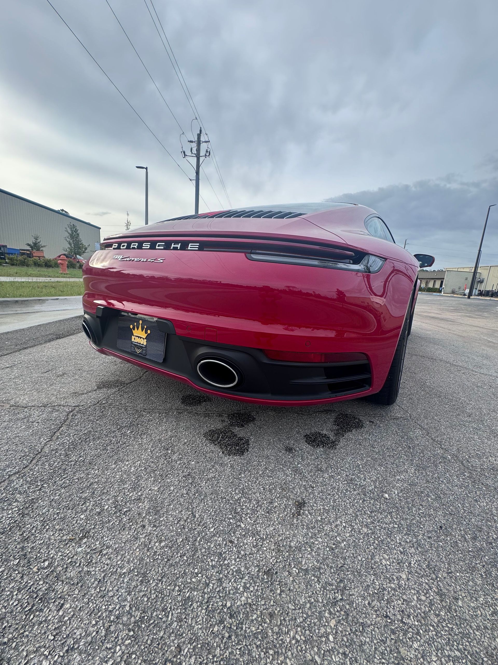 Red sports car on gravel in front of a cloudy sky.