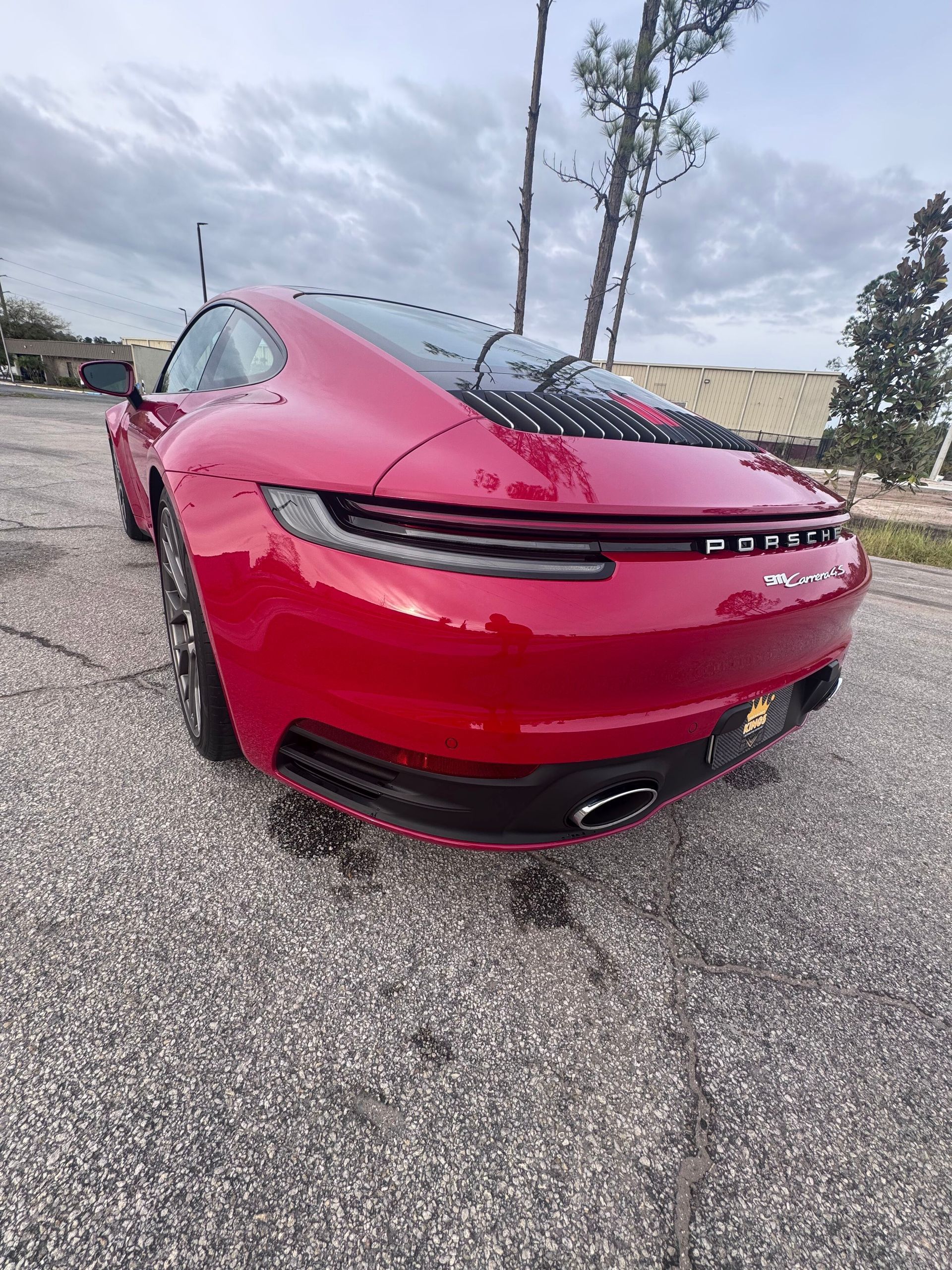 Red Porsche 911 rear view, parked on asphalt, under a cloudy sky.