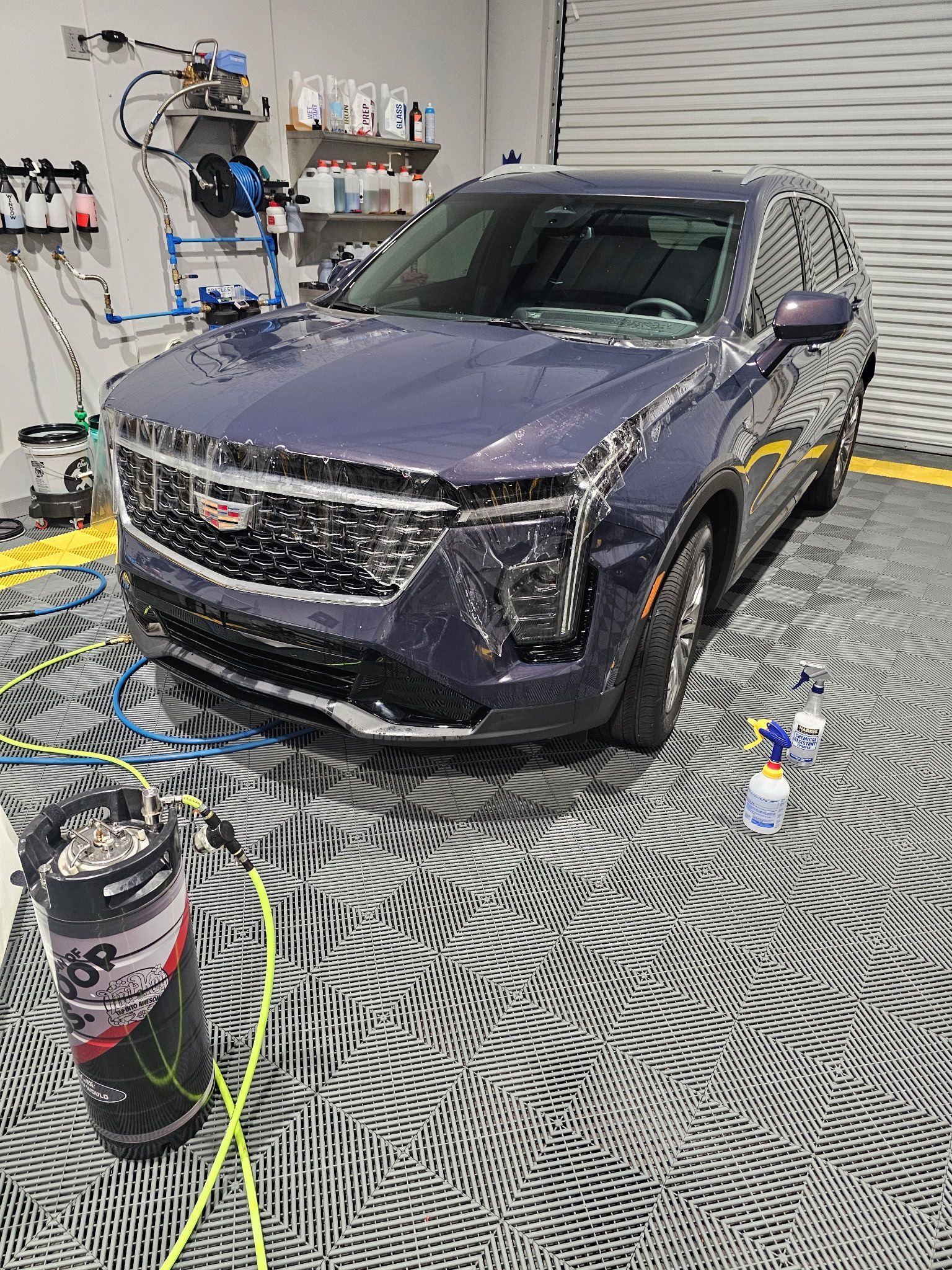 A blue Cadillac SUV is being washed in a garage, covered in soap.
