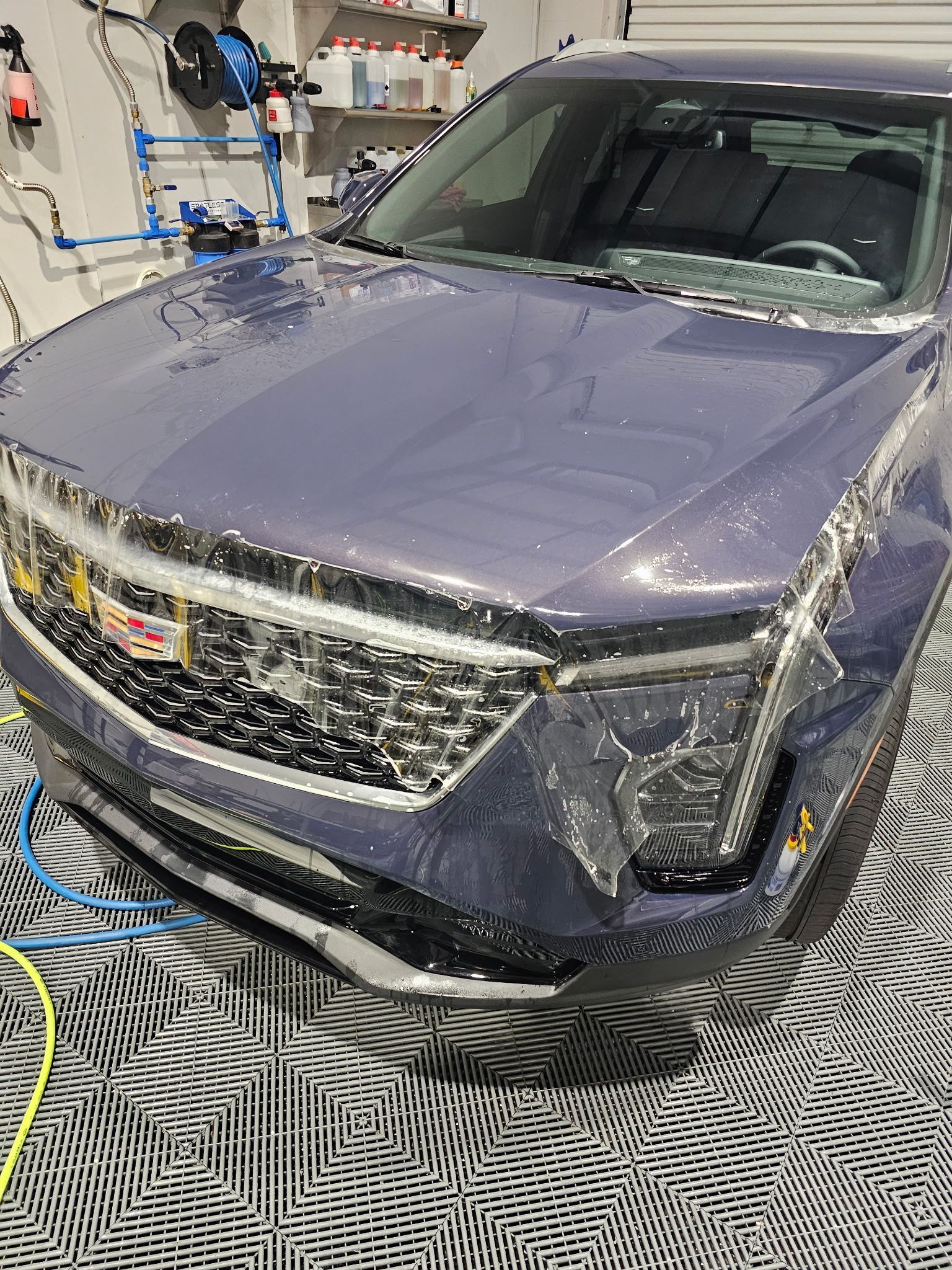 Blue GMC SUV being washed with foamy soap in a detail shop.