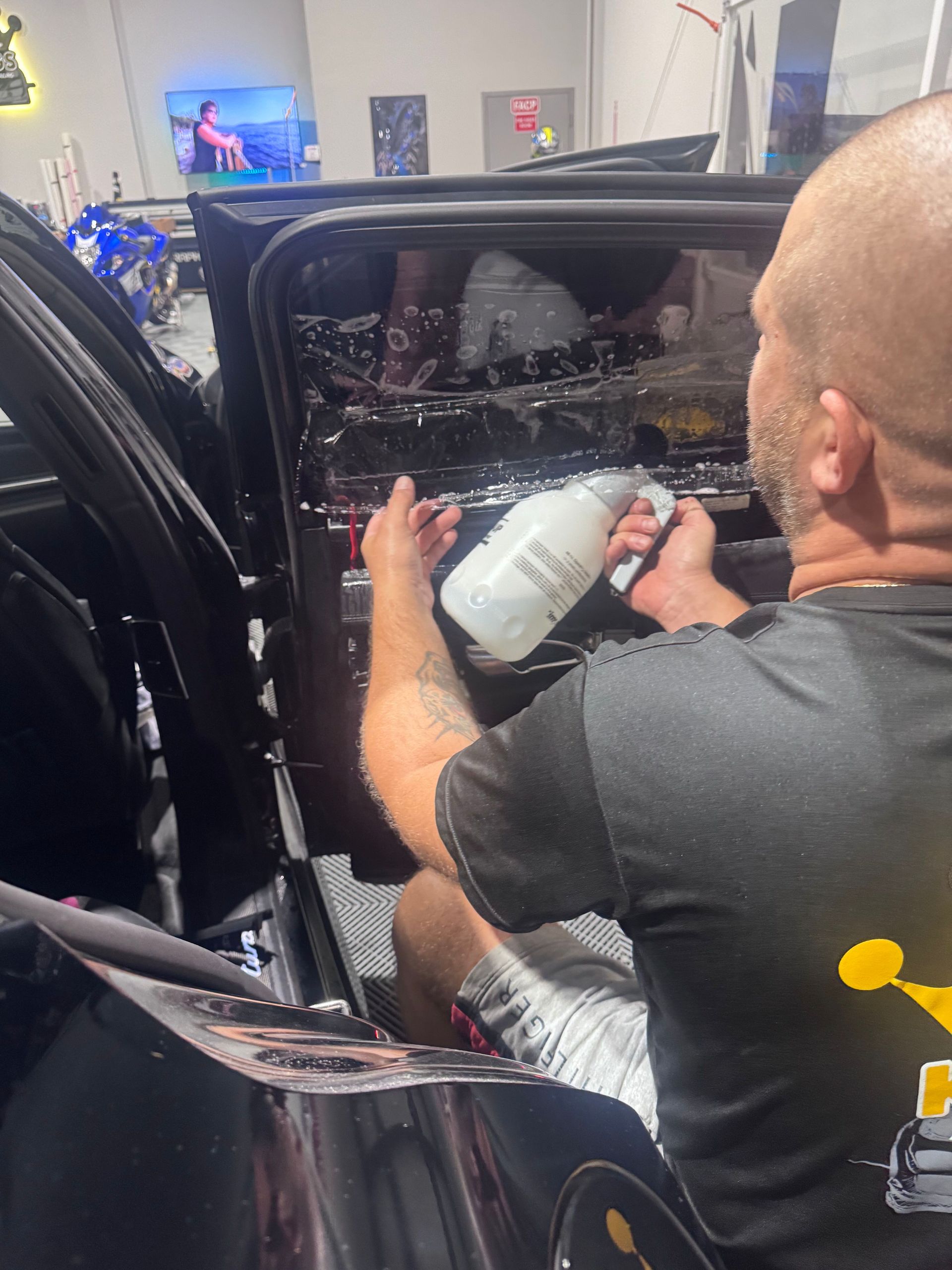 Man applying tint to a car window with a spray bottle inside a shop.