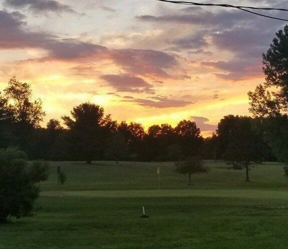 A sunset over a golf course with trees in the foreground