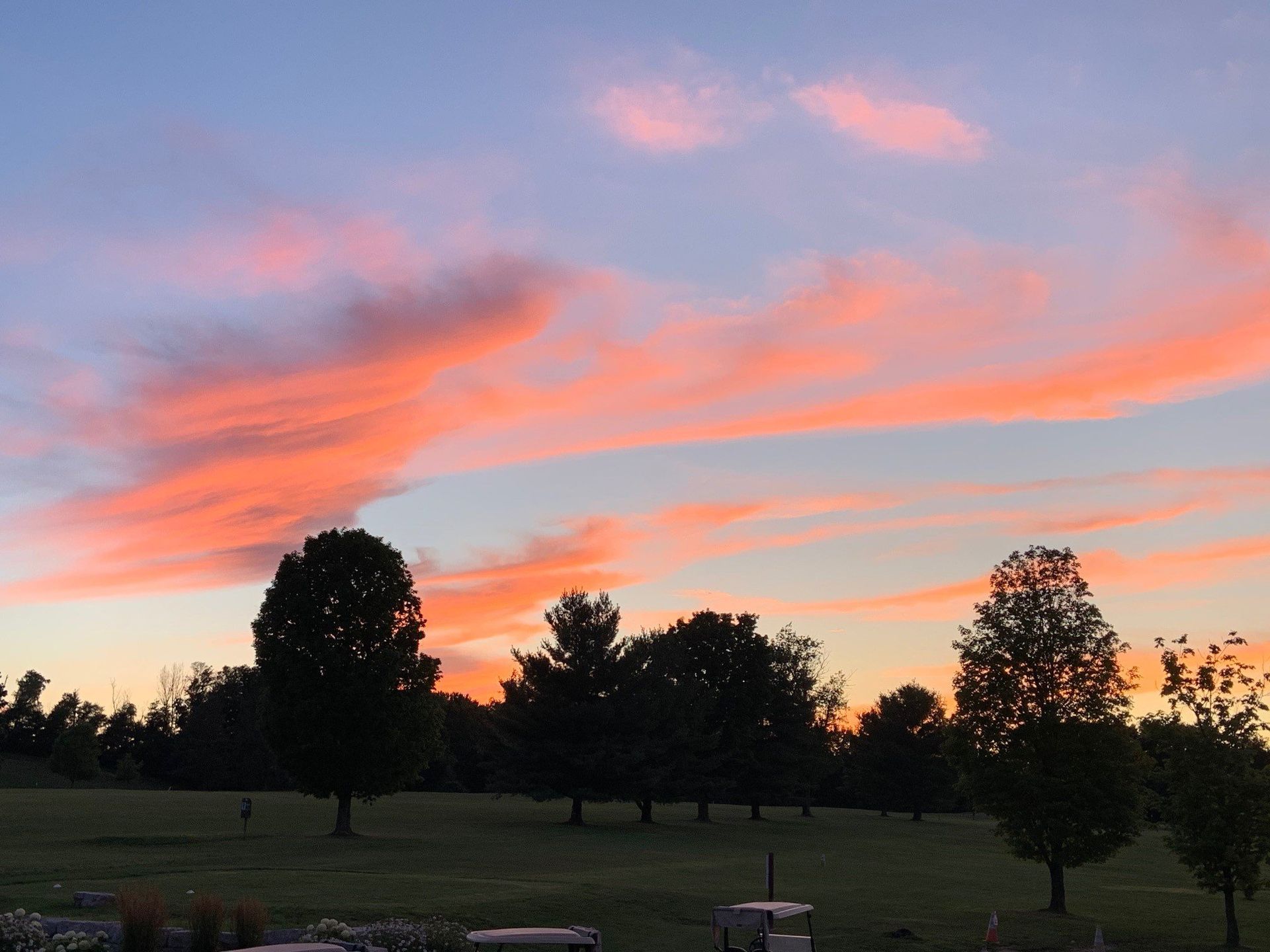 A sunset over a golf course with trees in the foreground