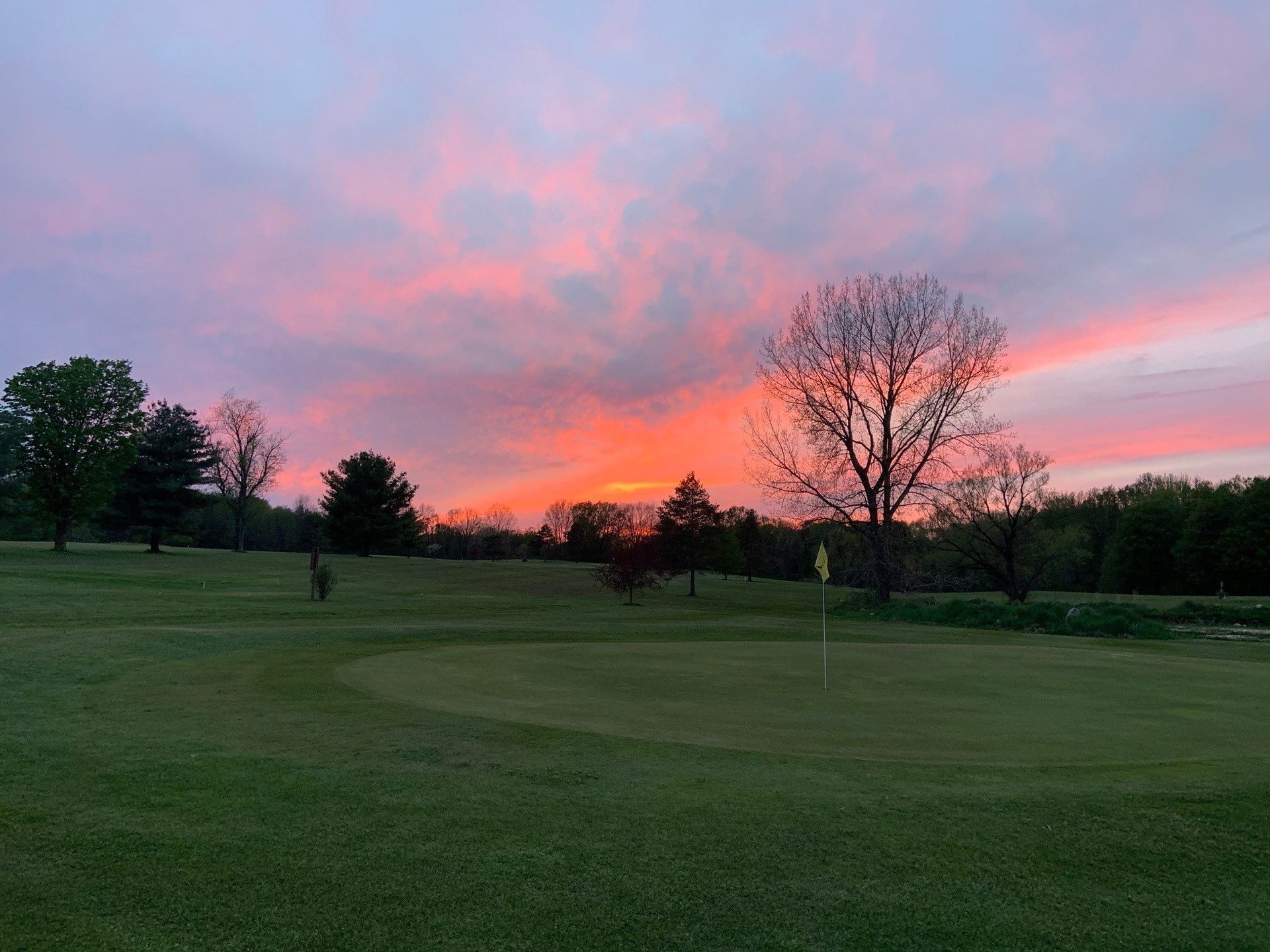 A sunset over a golf course with trees in the foreground.