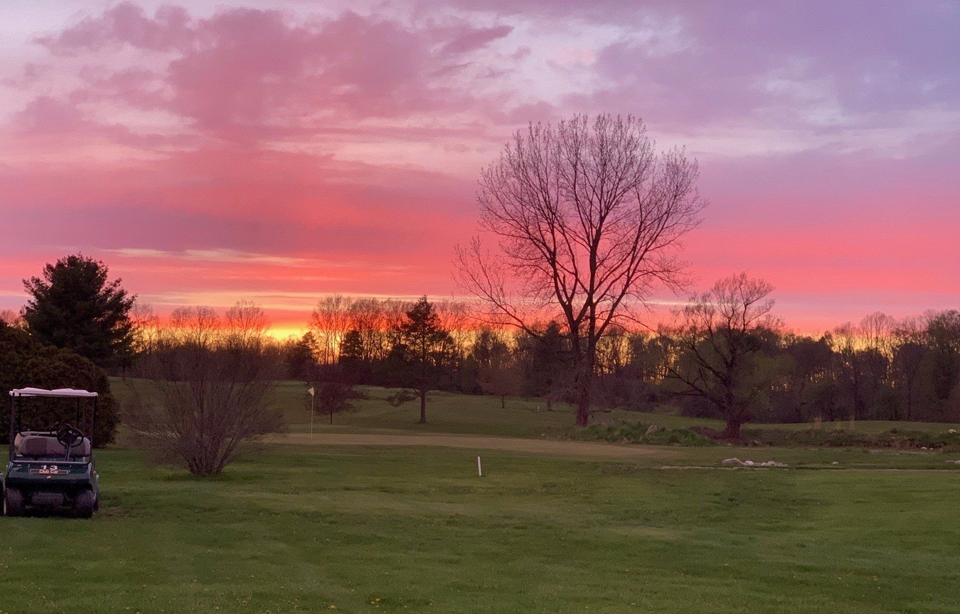 A golf cart is parked on a golf course at sunset.