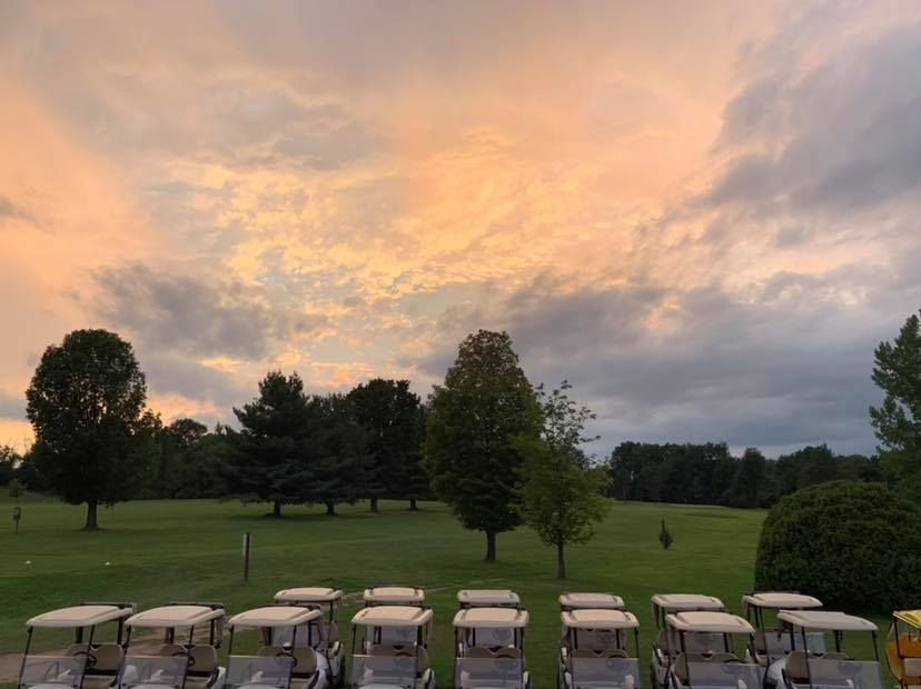 A row of golf carts are parked on a golf course at sunset.