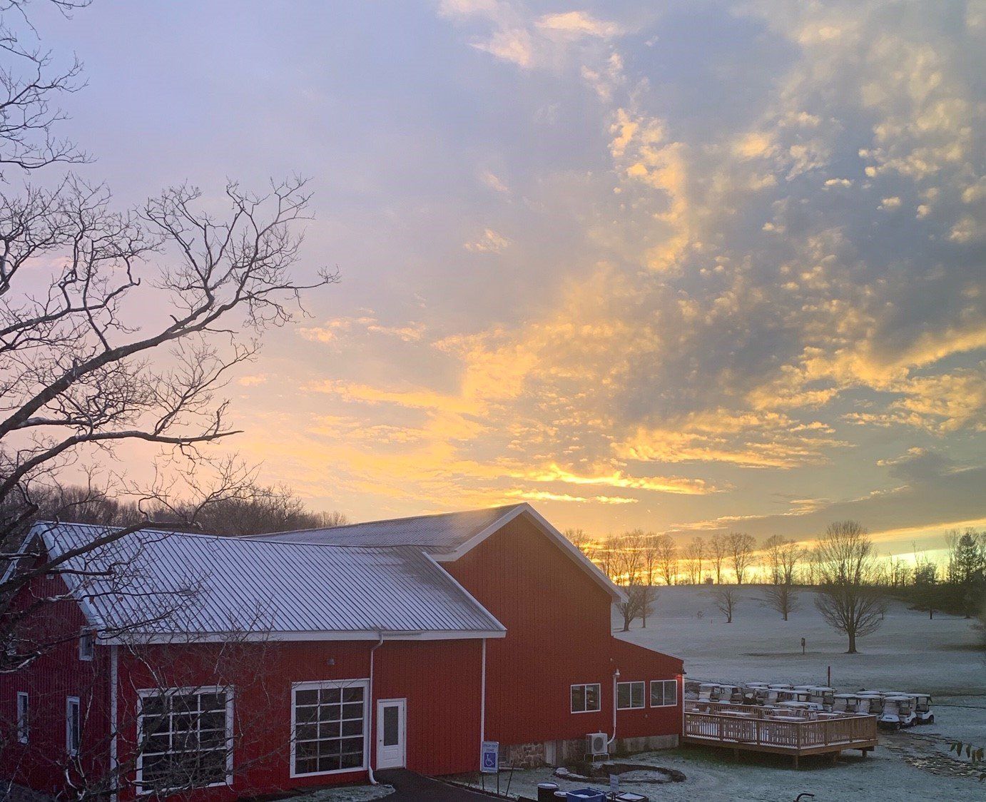 A red barn with snow on the roof at sunset
