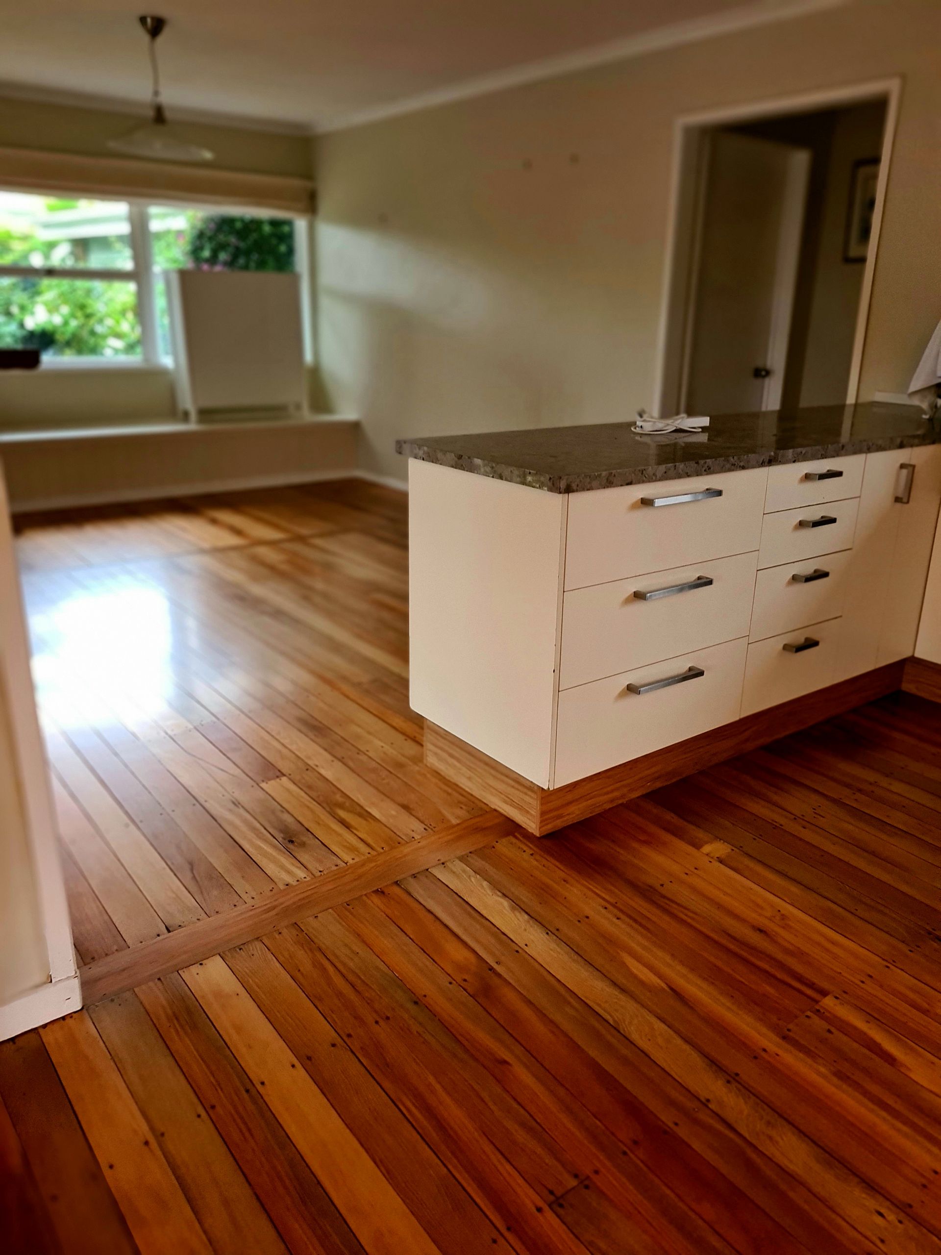 An empty kitchen with wooden floors and white cabinets.