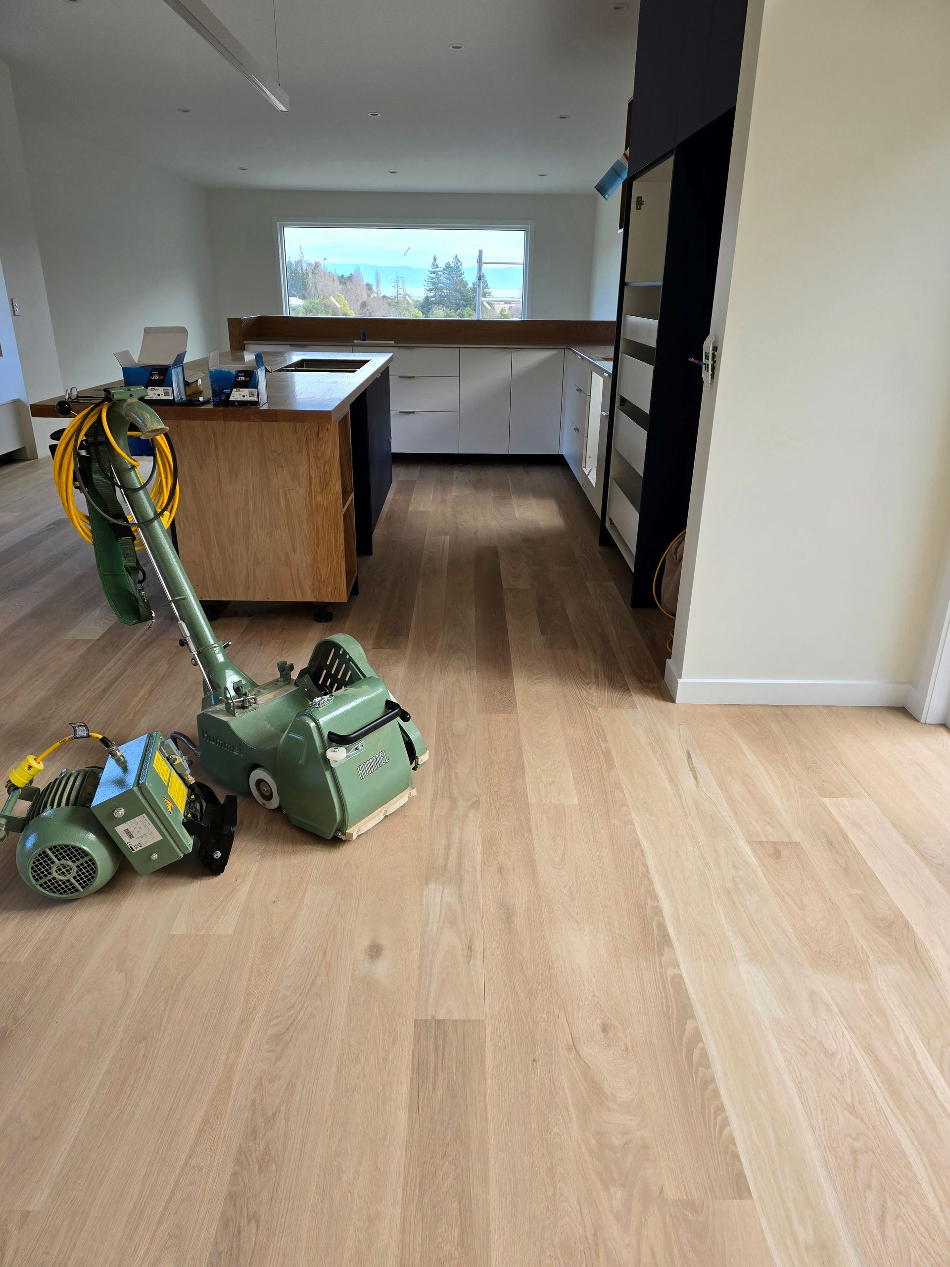 A floor sander is sitting on a wooden floor in a kitchen.