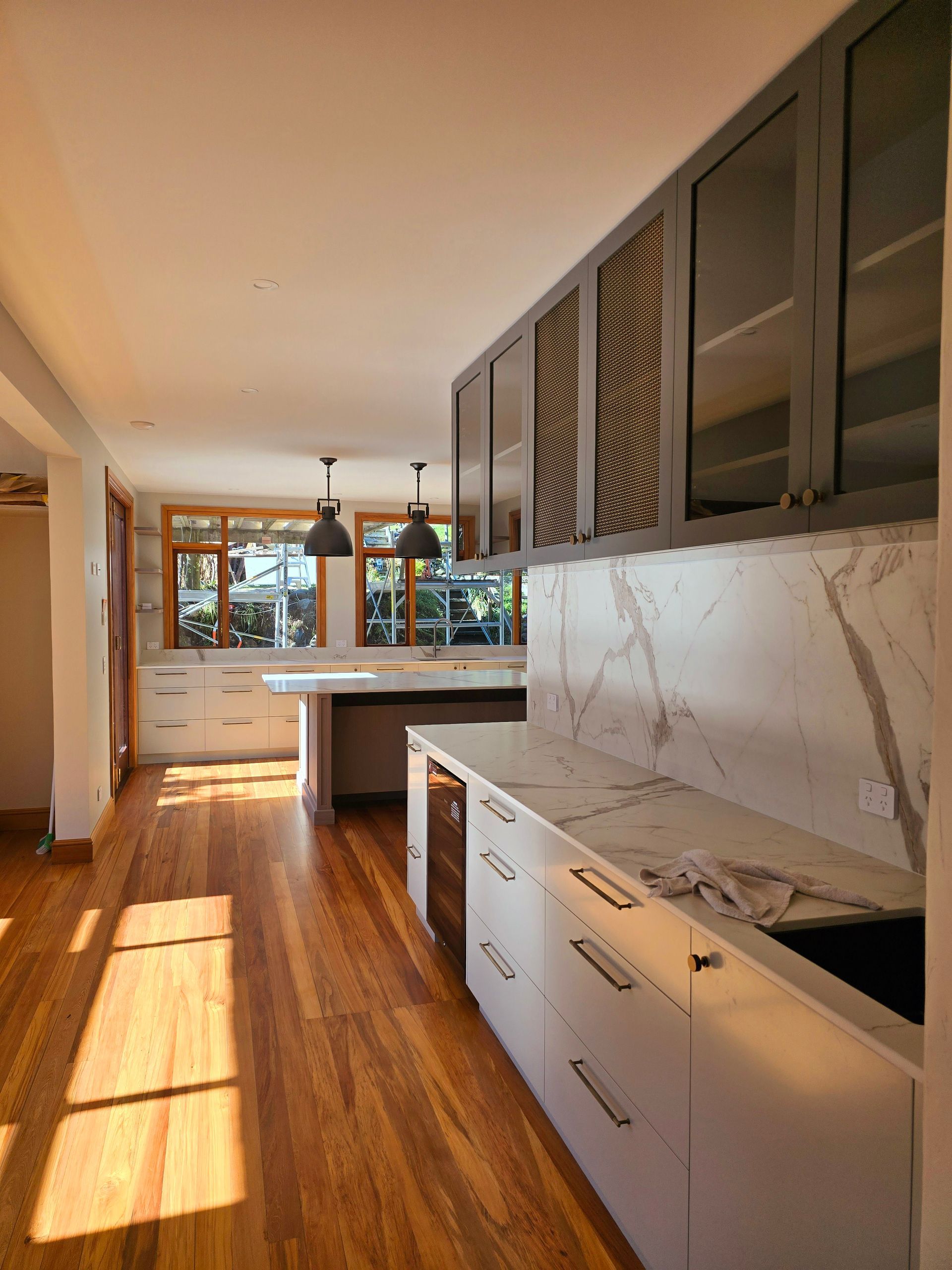 A kitchen with wooden floors , white cabinets and marble counter tops.