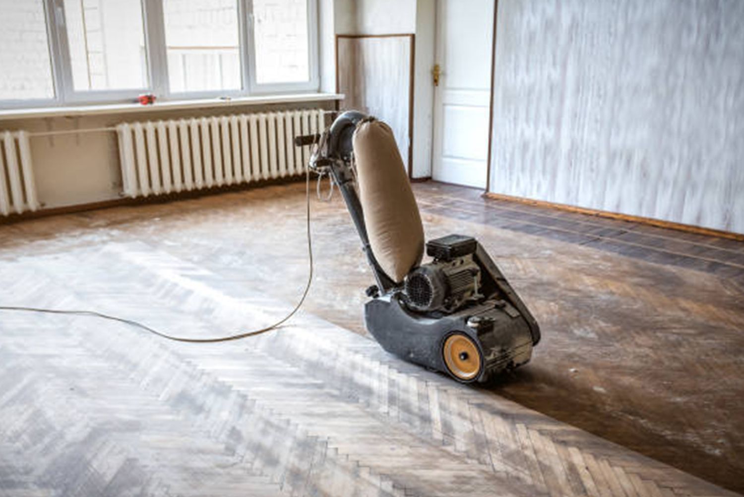 A machine is sanding a wooden floor in an empty room.