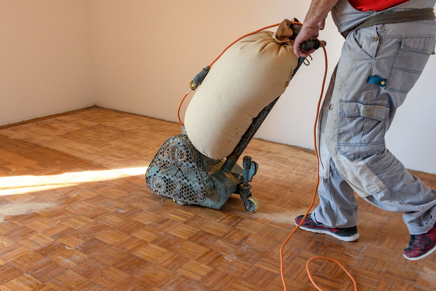 A man is sanding a wooden floor with a machine.