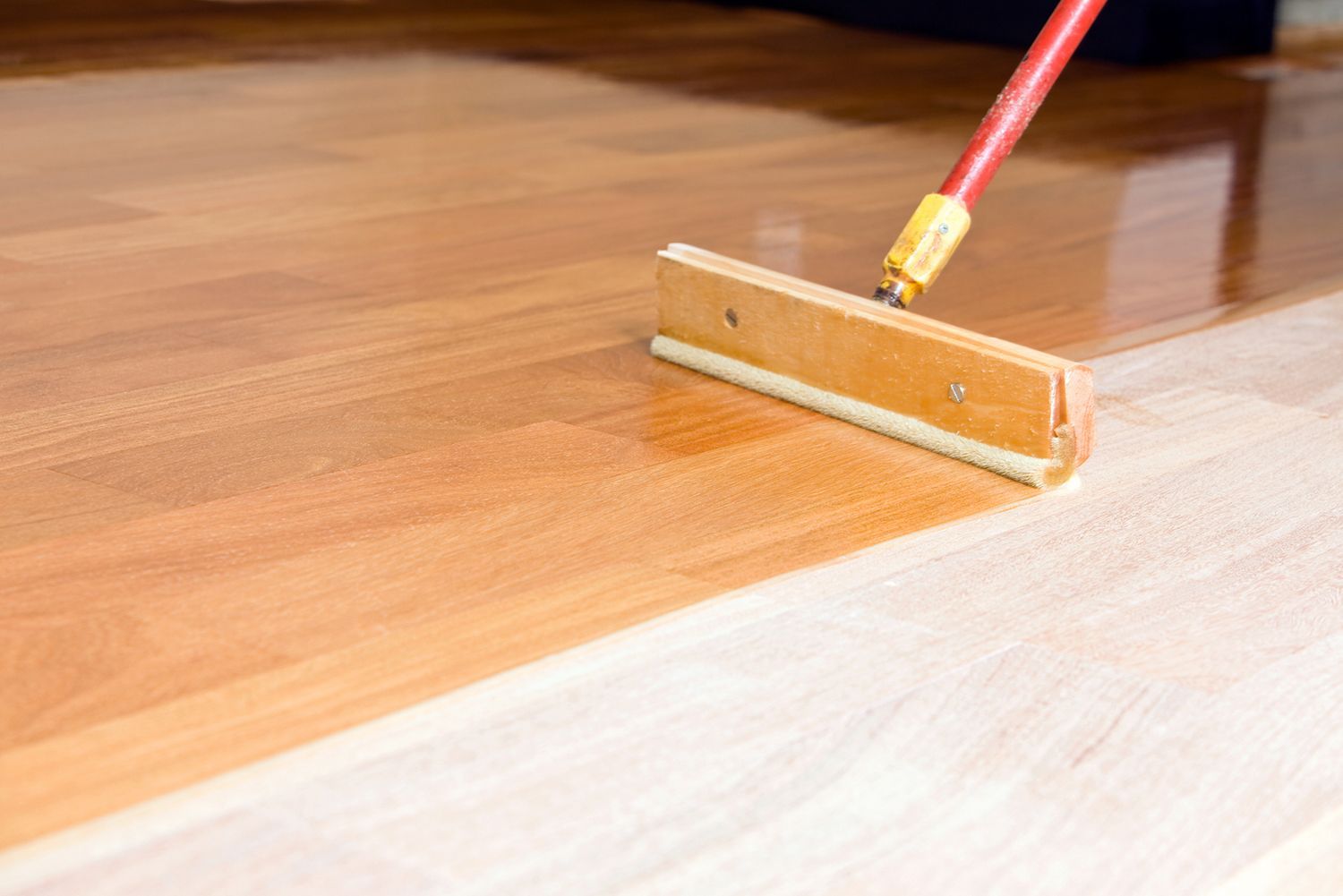 A person is painting a wooden floor with a roller.
