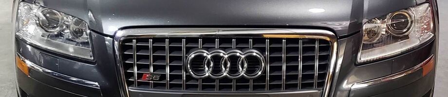 Front view of a dark gray Audi car featuring the signature four-ring emblem and an S-line badge on the front grille. | Allroad Motorsports