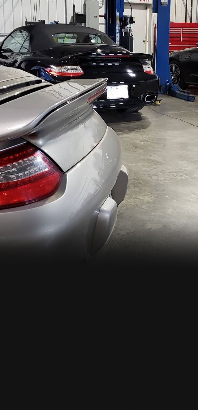 Rear views of a silver and a black Porsche convertible parked inside an auto repair shop. |  Allroad Motorsports