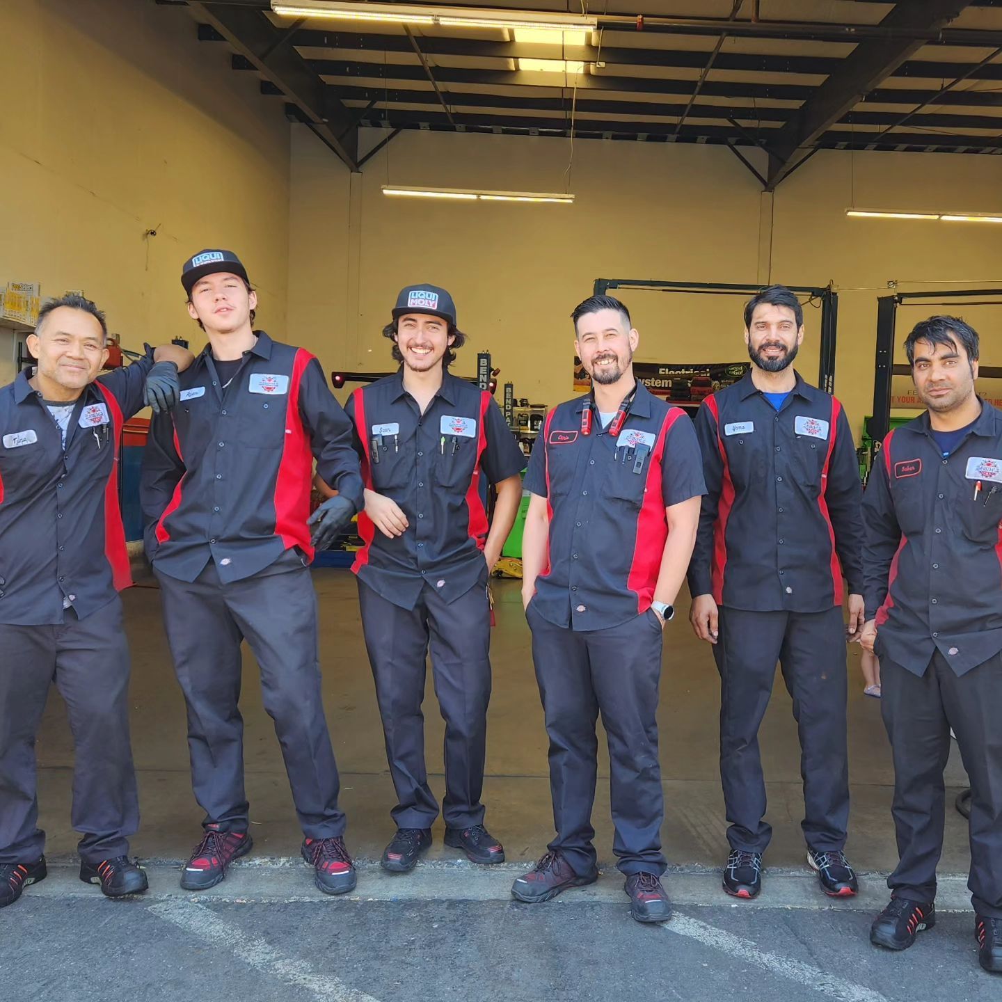 Mechanics in black and red uniforms pose in front of a garage | Freebird Automotive