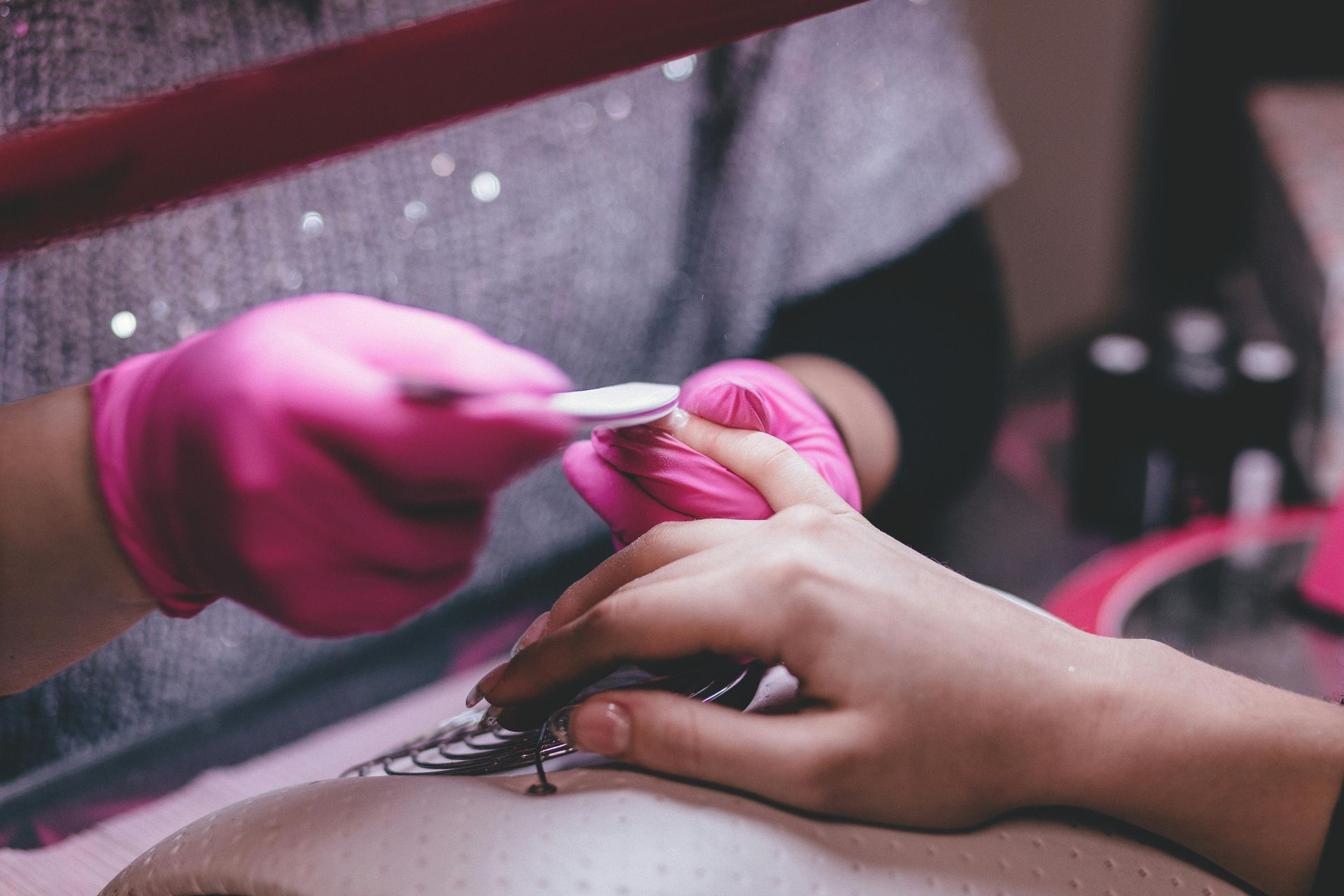 Person getting a manicure; pink gloved hands filing a fingernail.