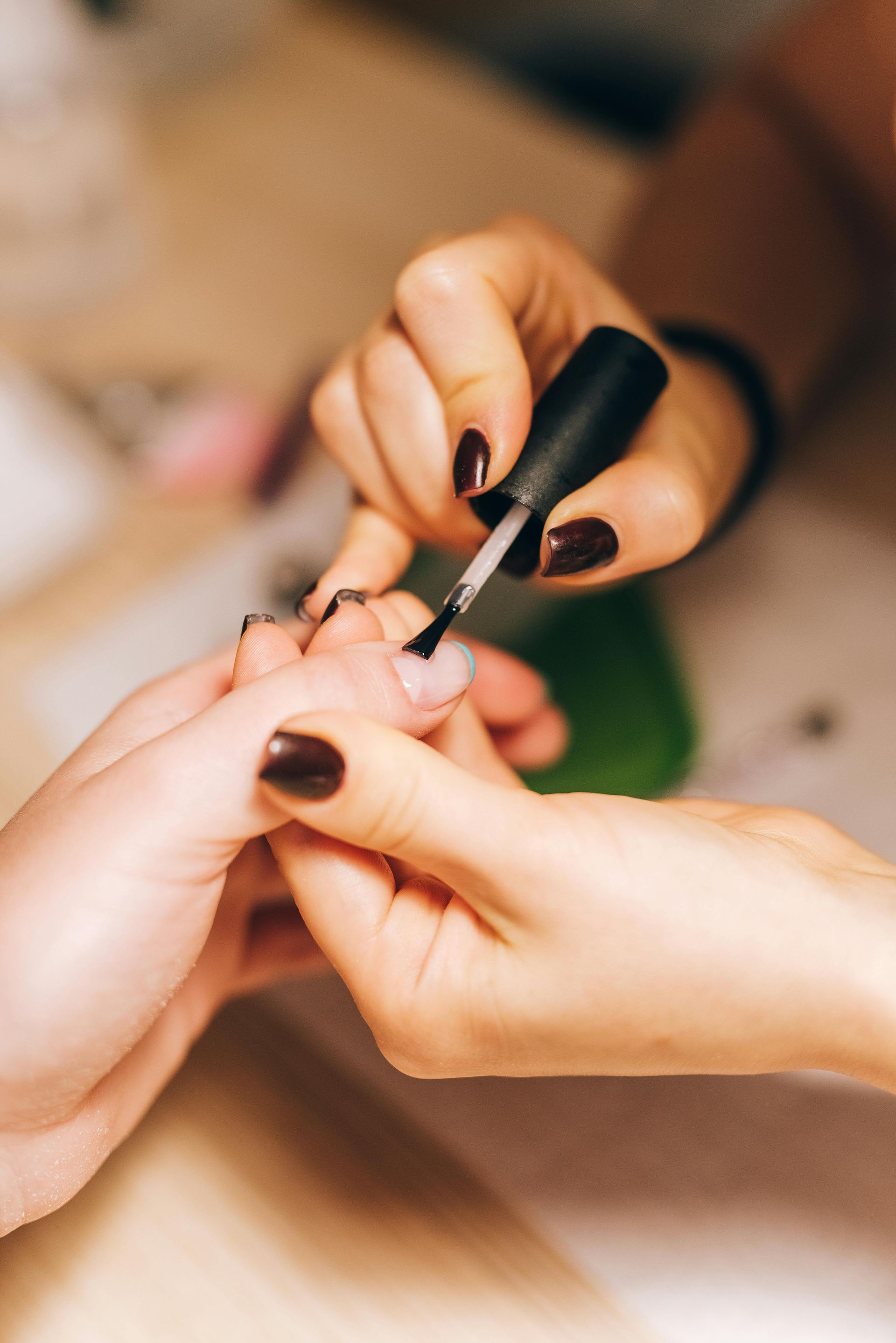 A hand applying dark nail polish to another person's fingernails.