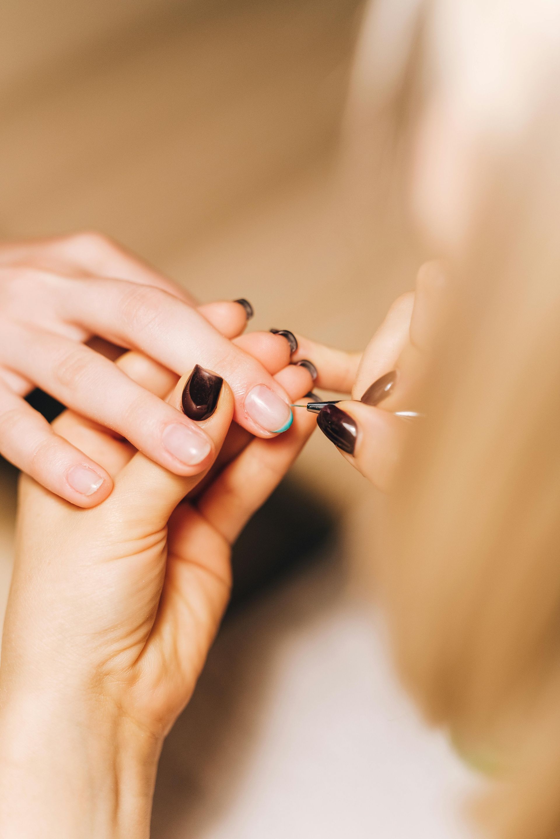 Person's hand getting fingernails painted dark blue by another person's hand. Focus on the nails.