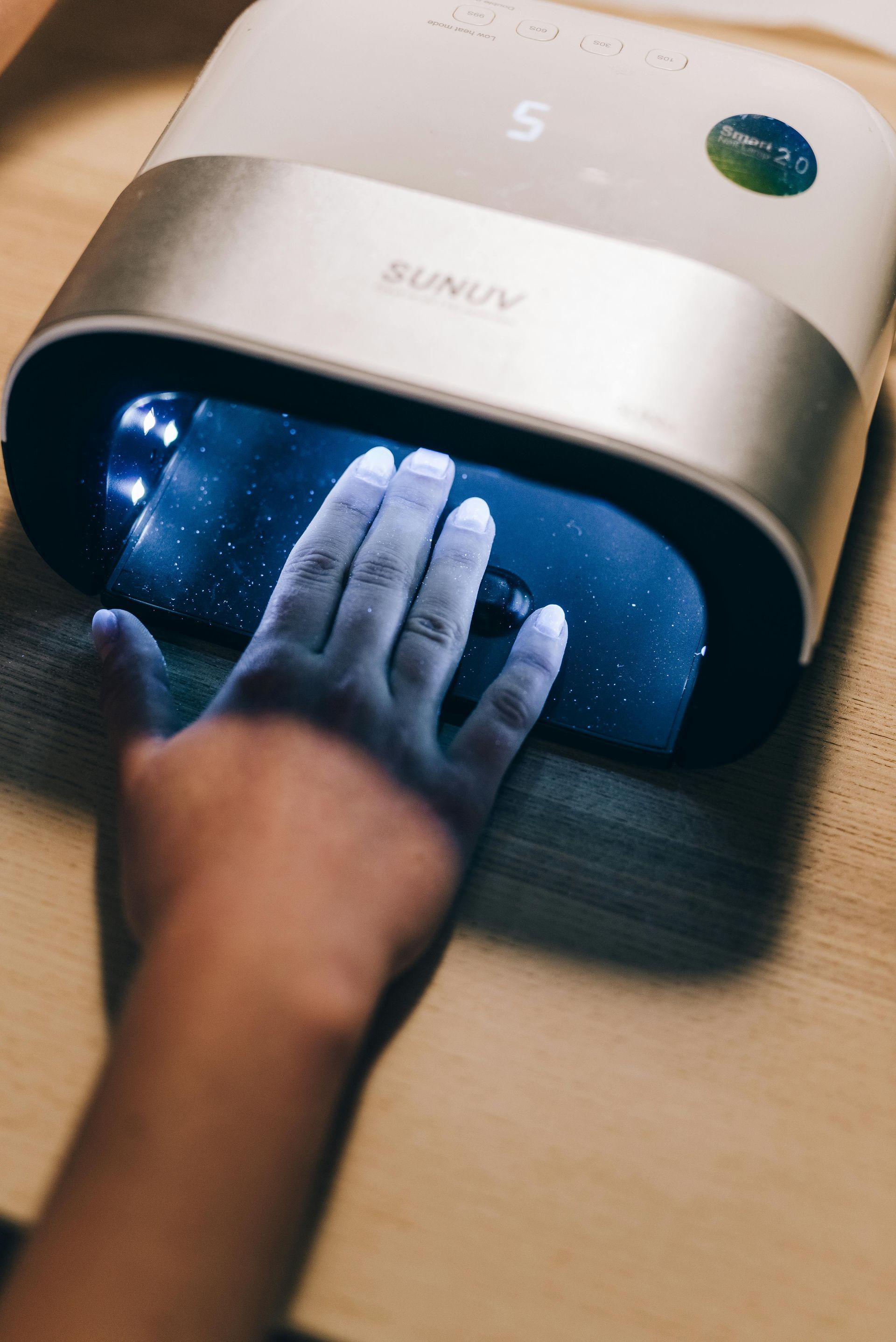 Hand under a UV nail lamp; white fingernails. Blue light emitting from the lamp.