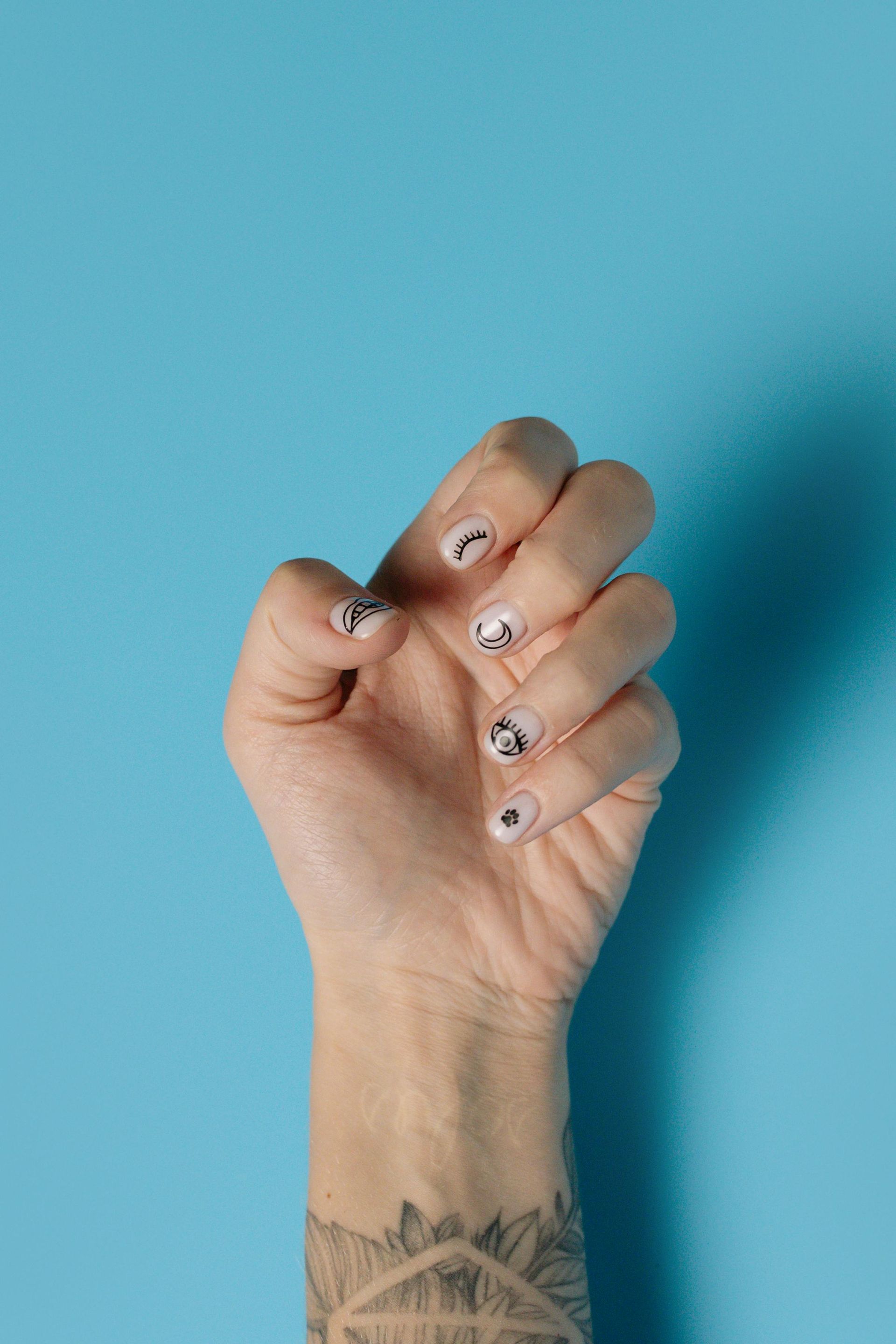 Hand with black and white patterned nails and a forearm tattoo, against a blue background.