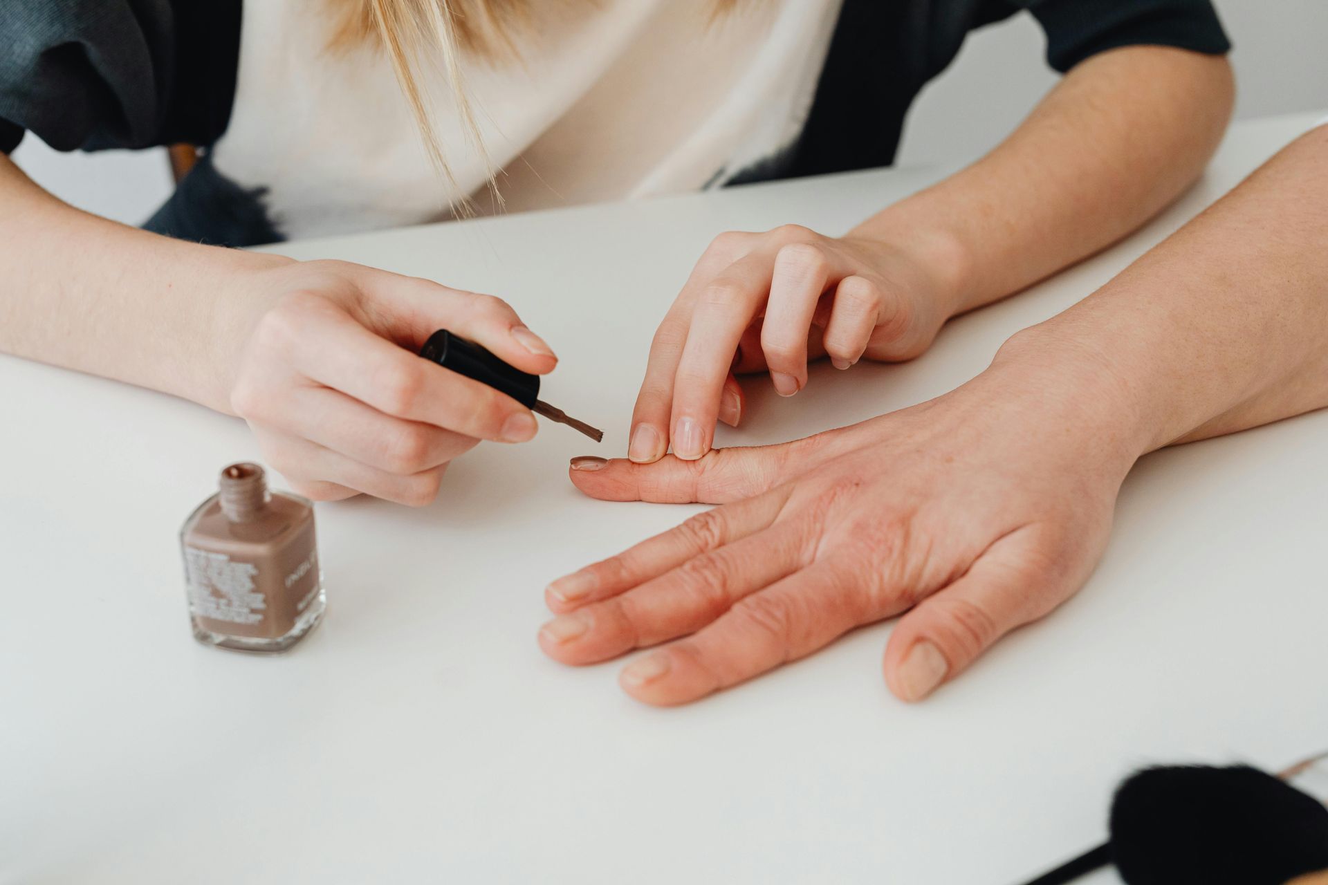 Person applying brown nail polish to another person's fingernails.