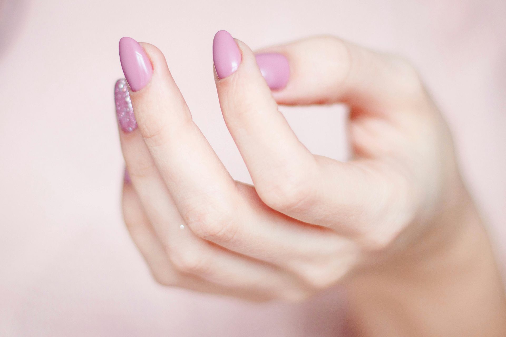 Hand with pink almond-shaped nails, slightly curved, against a pink background.