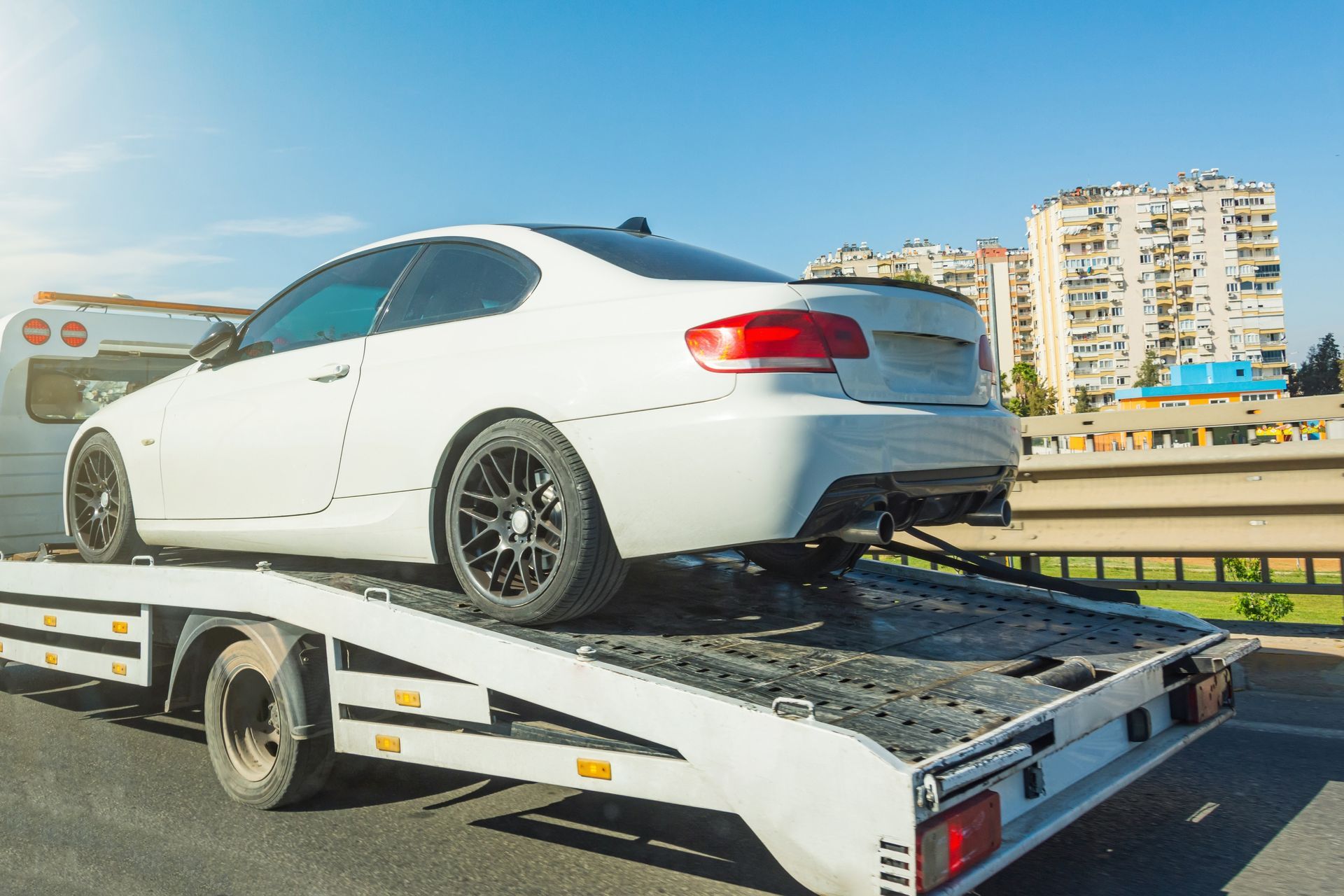 White Coupe Car Secured On Flatbed Tow Truck City Background — Penfold Towing in Burrum Heads, QLD
