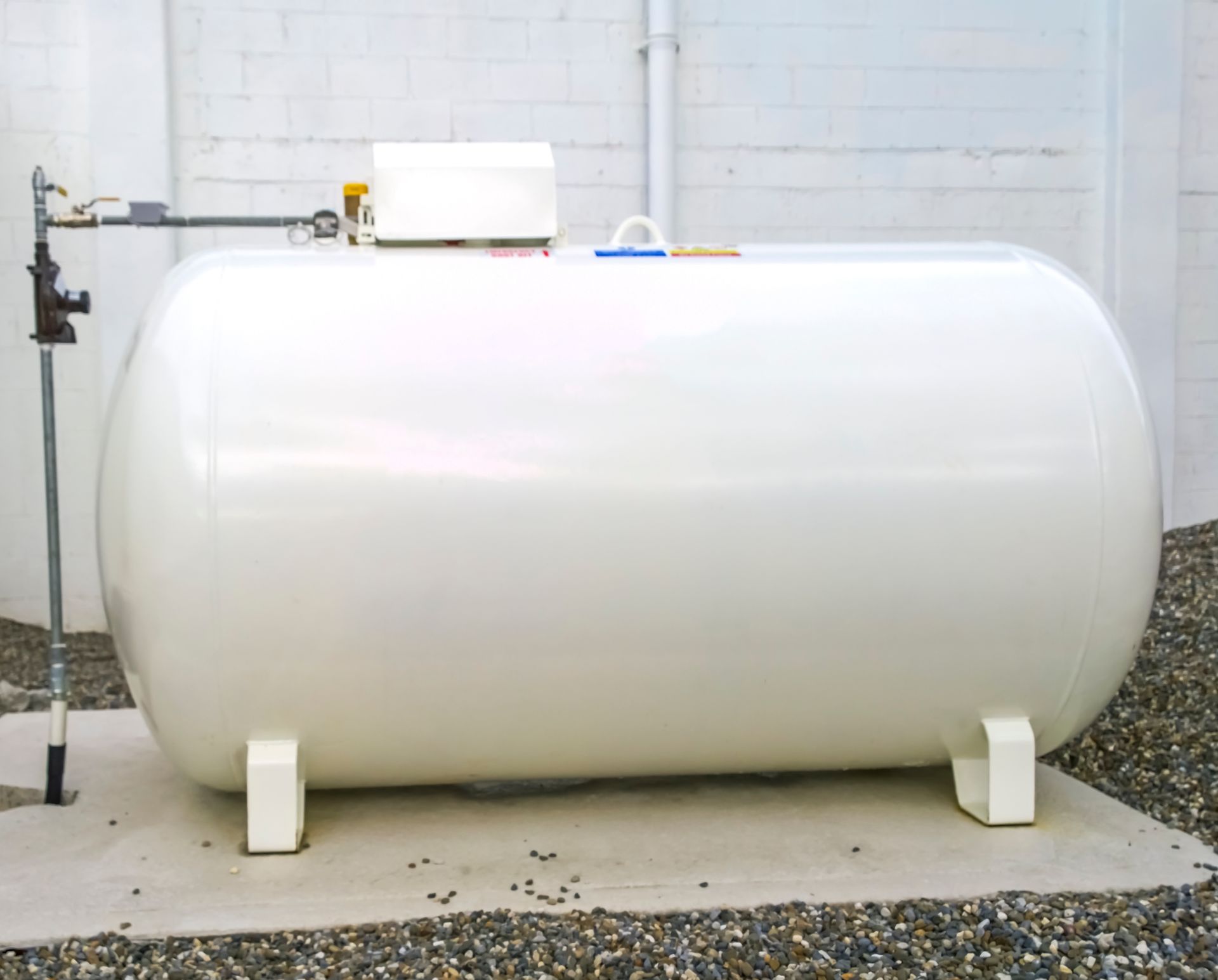 A large propane tank is sitting in the grass next to a wooden fence.
