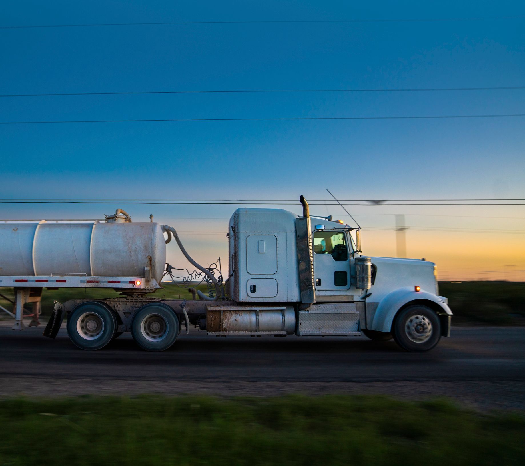 A semi truck is driving down a road at sunset.