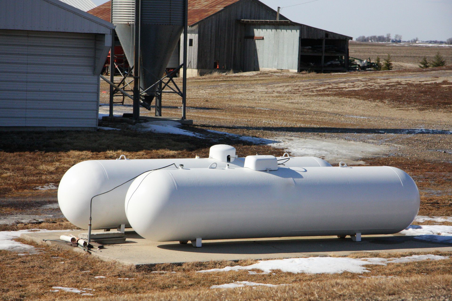 Two propane tanks are sitting in a field in front of a barn.