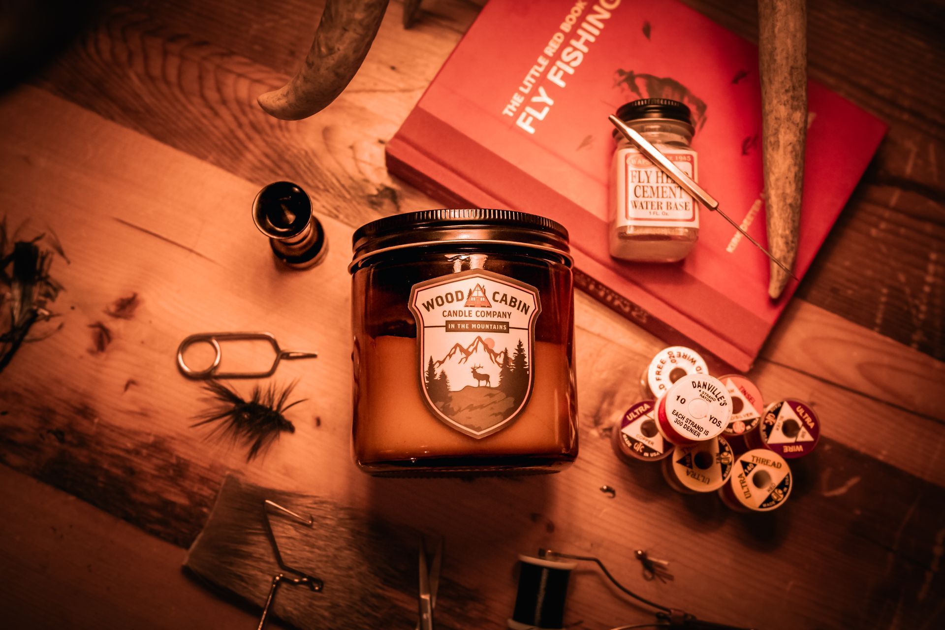 Still life of fly-fishing gear on a wood surface: candle, book, flies, tools, and dice.