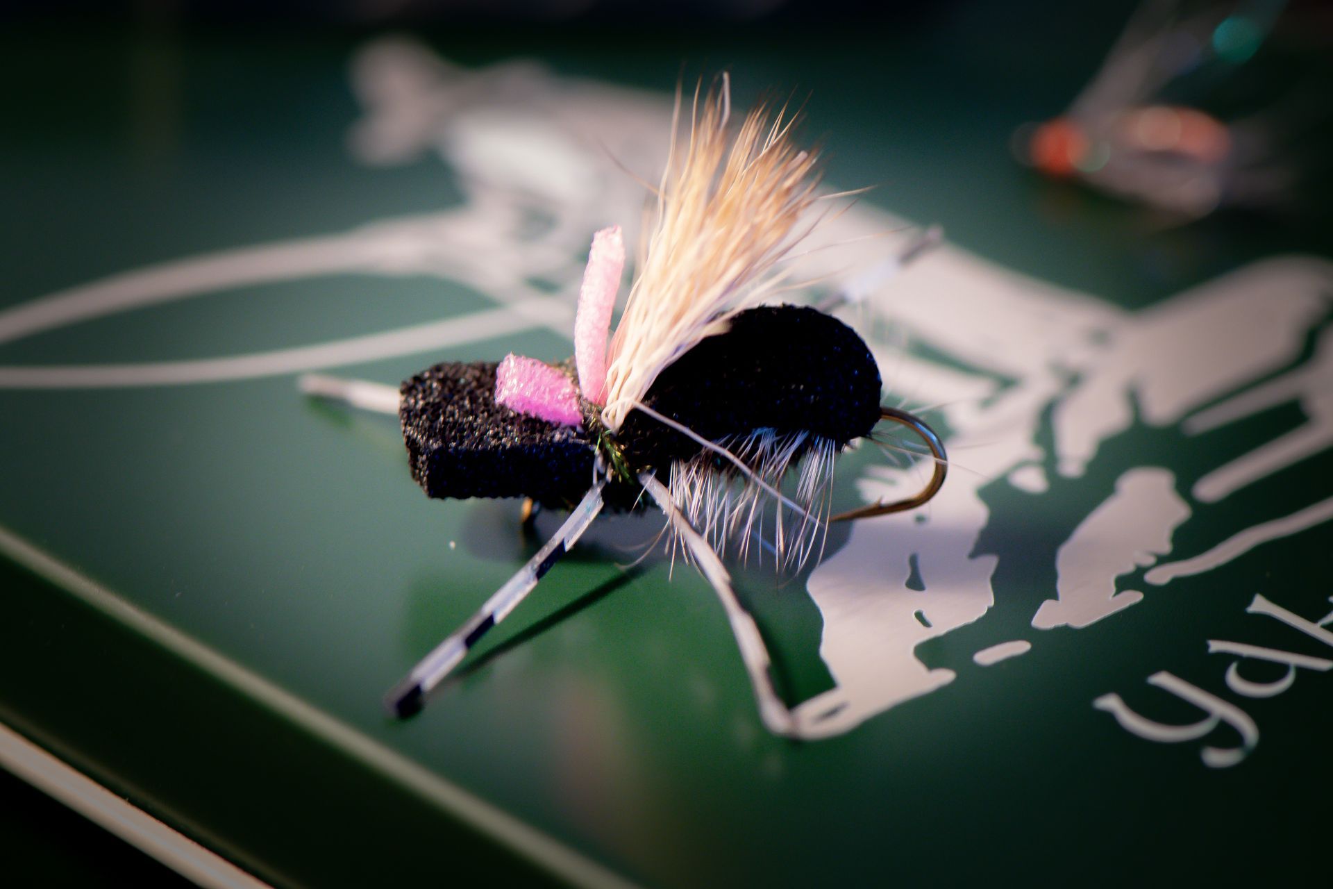 Close-up of a black and pink fishing fly with white and tan accents, resting on a green surface.