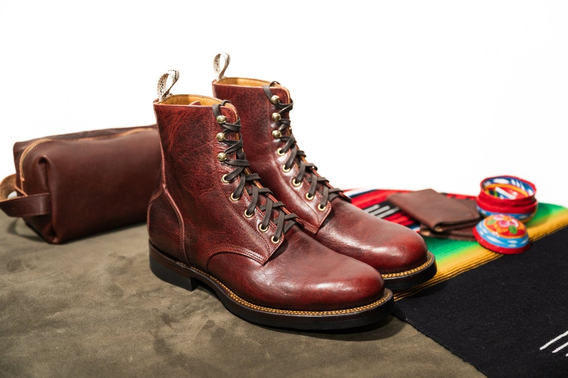 Pair of brown leather boots with a toiletry bag, wallet, and colorful accessories on a blanket.