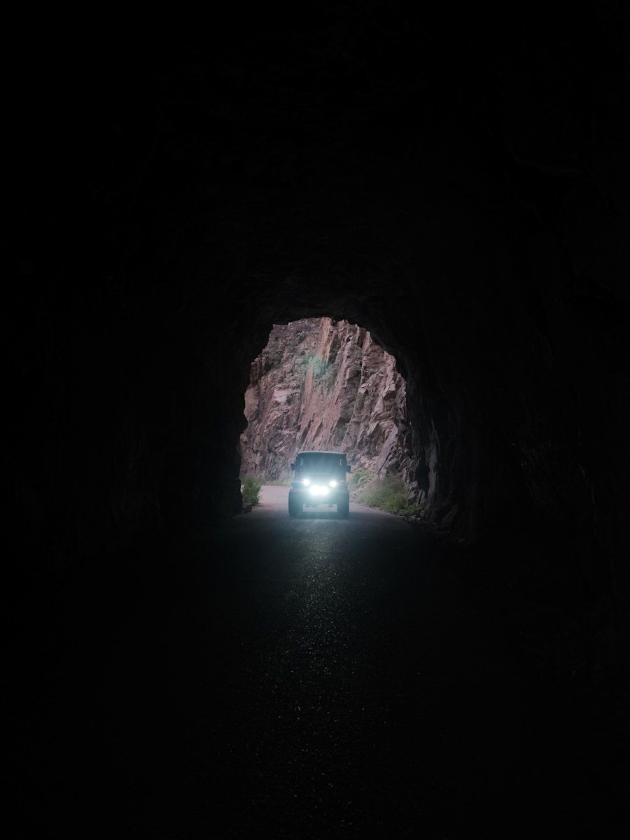 Car approaching from within a dark tunnel; bright headlights illuminate the road.