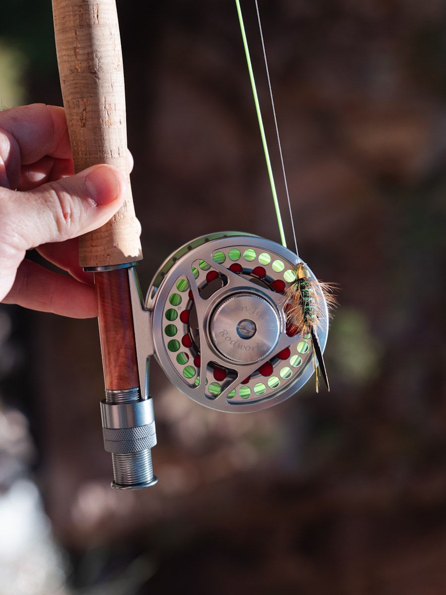 Fly fishing rod with reel, line, and a fly. Cork handle held by hand.