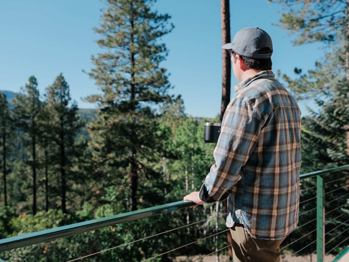 Man on a balcony with a coffee cup looking at a forest view.