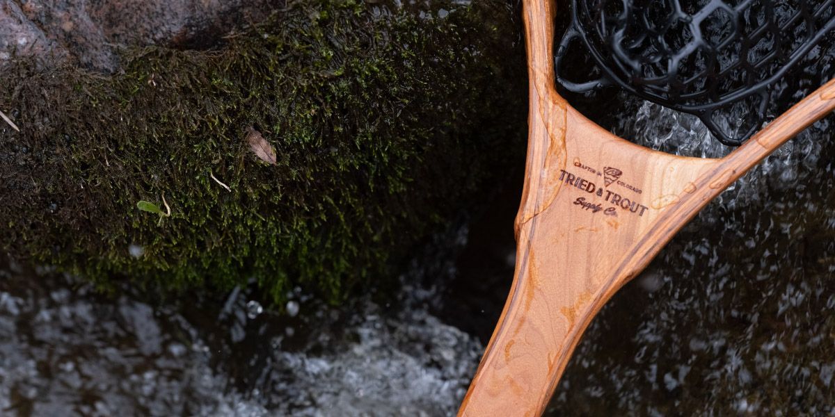 Wooden fishing net with moss-covered rocks and water in the background.
