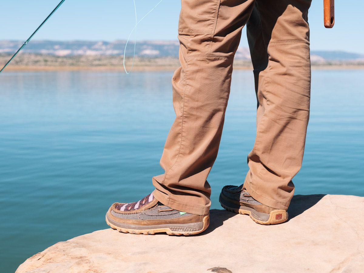 Person in brown pants and Twisted X shoes fishing by a lake.