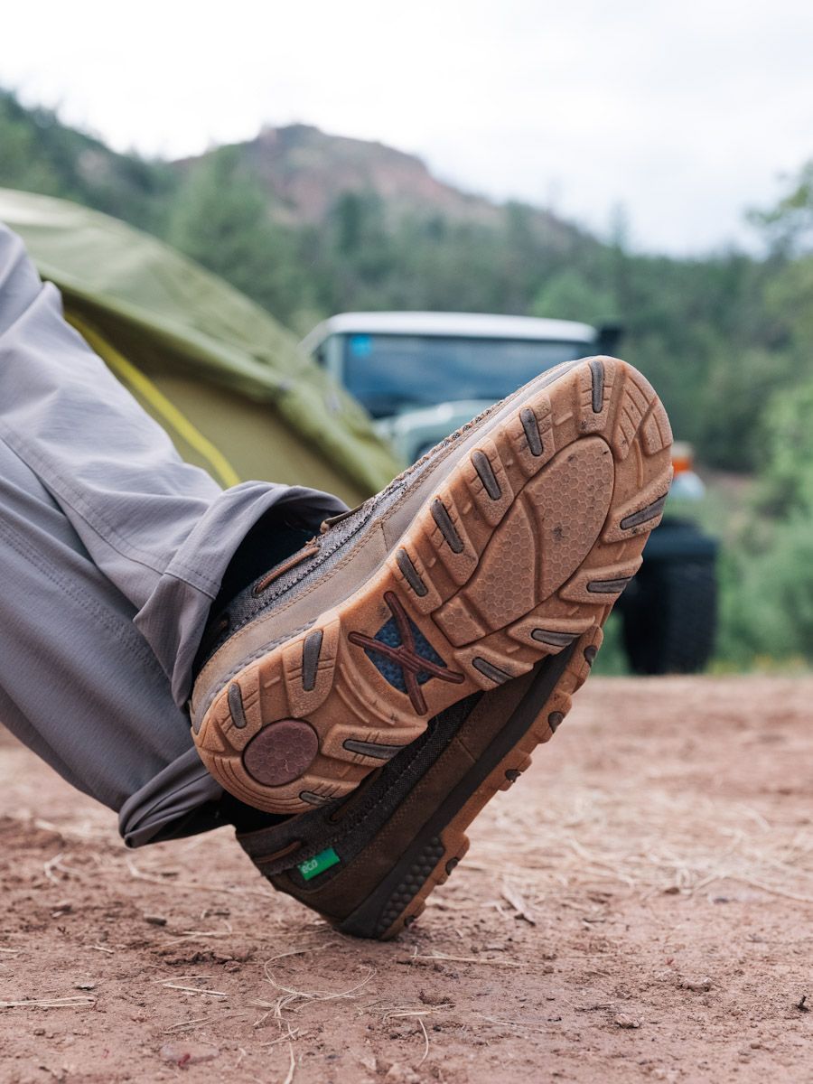 Person's brown hiking boots with rugged soles resting on the ground, in a camping setting.