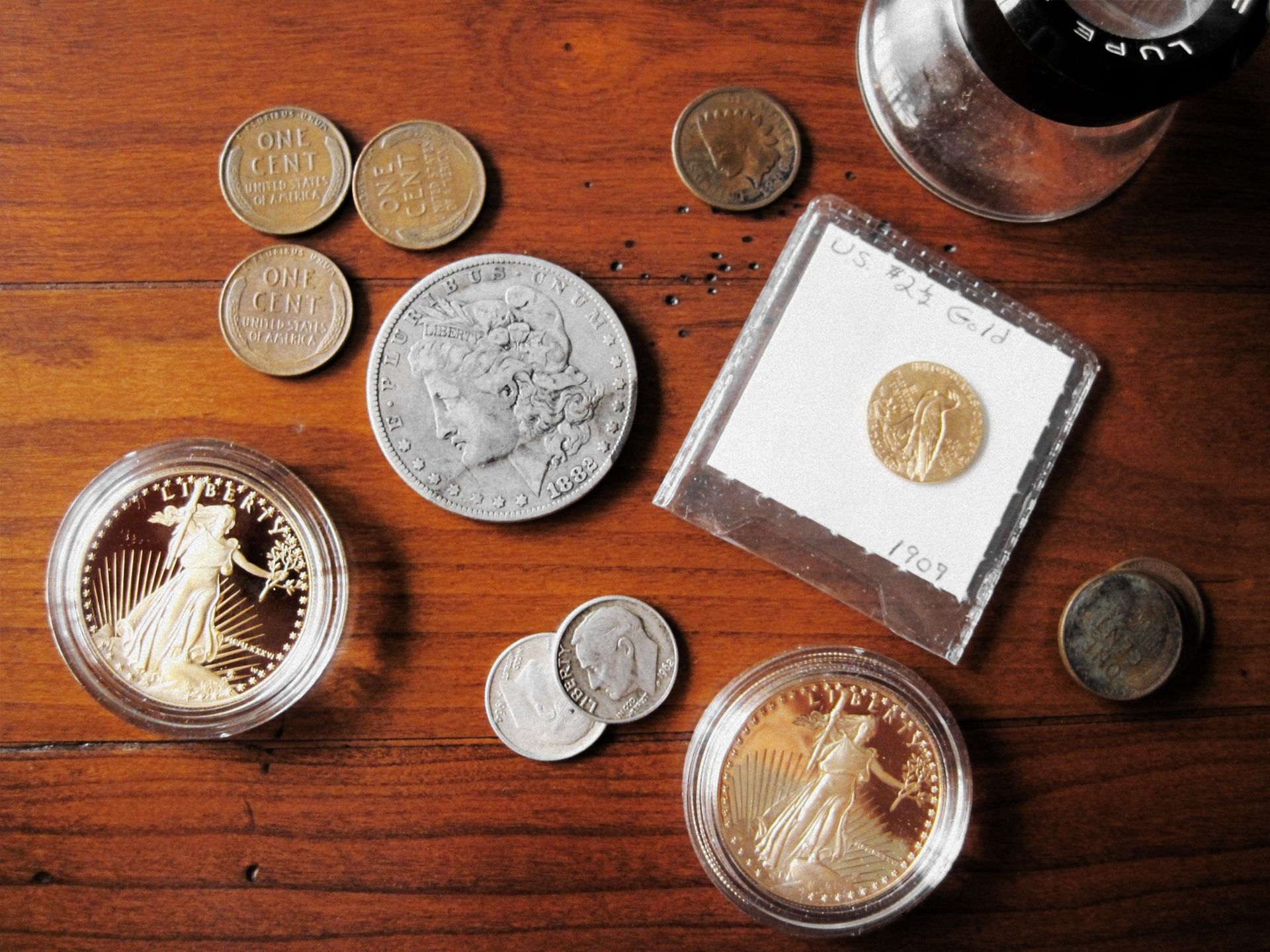 Assorted vintage coins and a magnifying glass displayed on a wooden surface for appraisal.