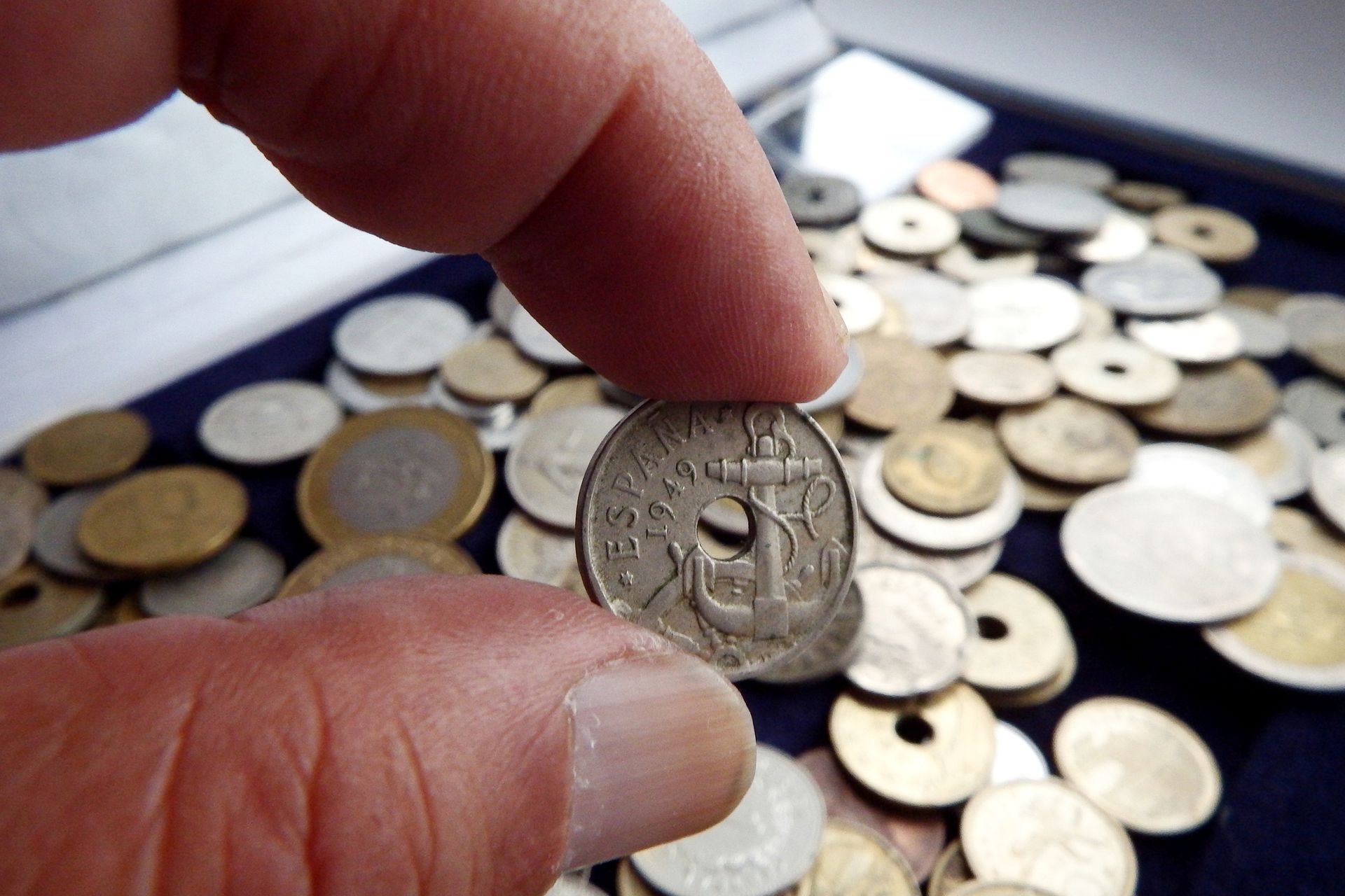 A person is holding a coin in their hand in front of a pile of coins.